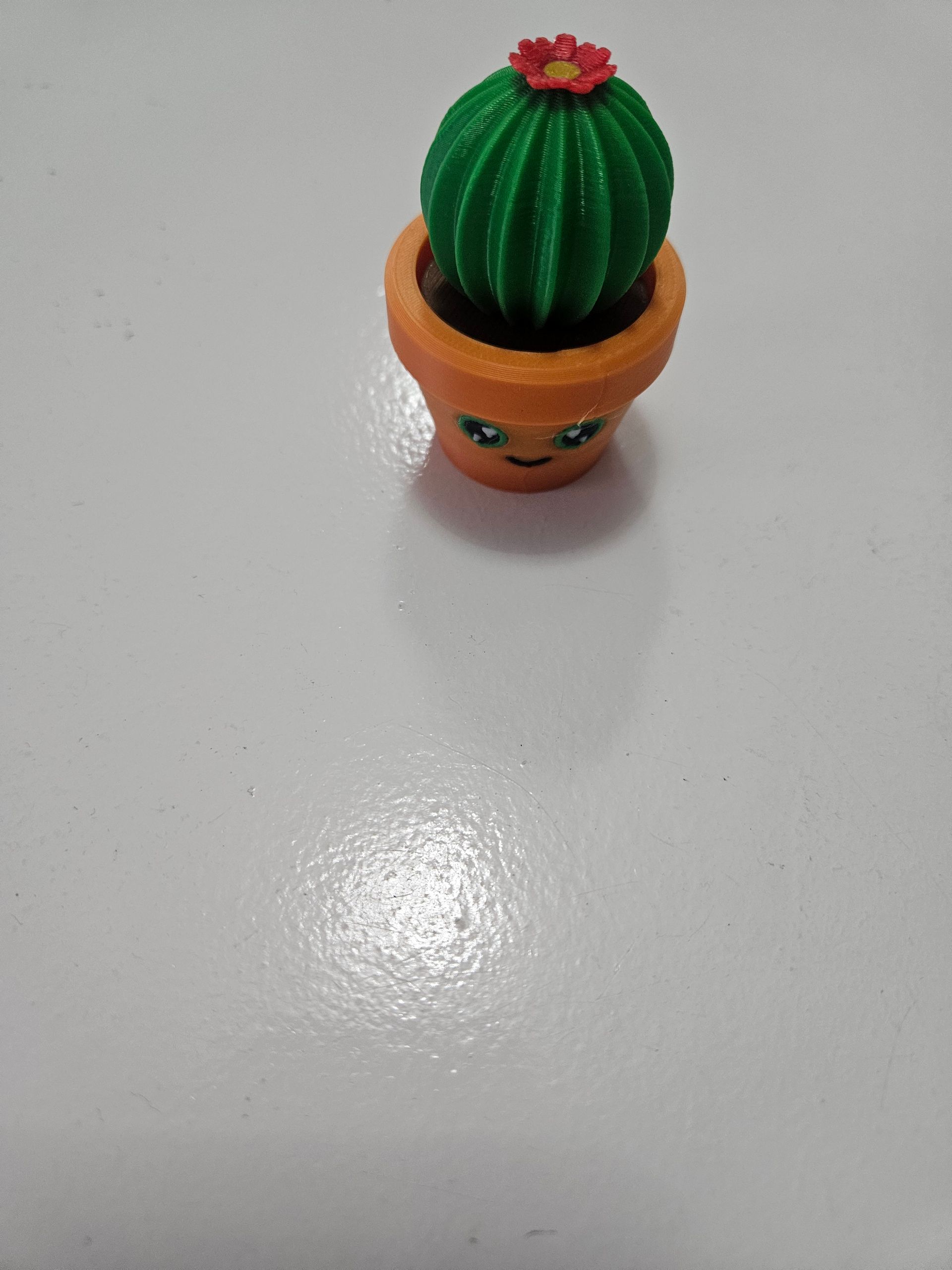 Small orange cactus toy pot with a red flower on a white surface