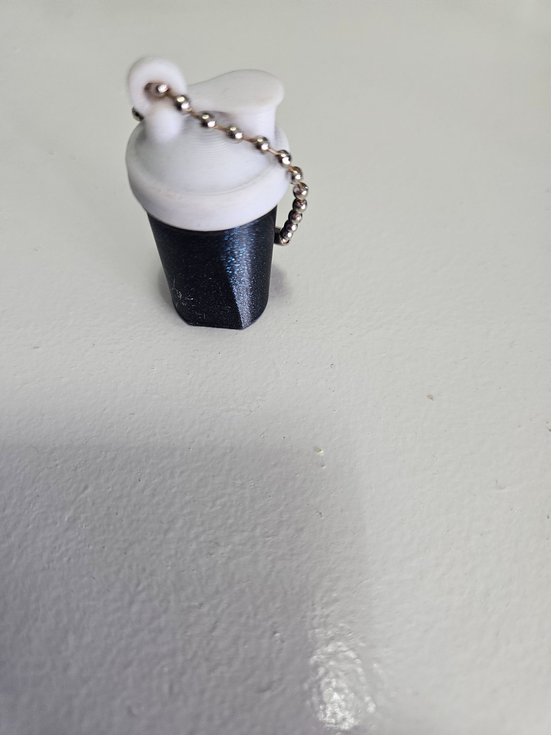 Small glittery black-and-white container with a silver chain on a light surface