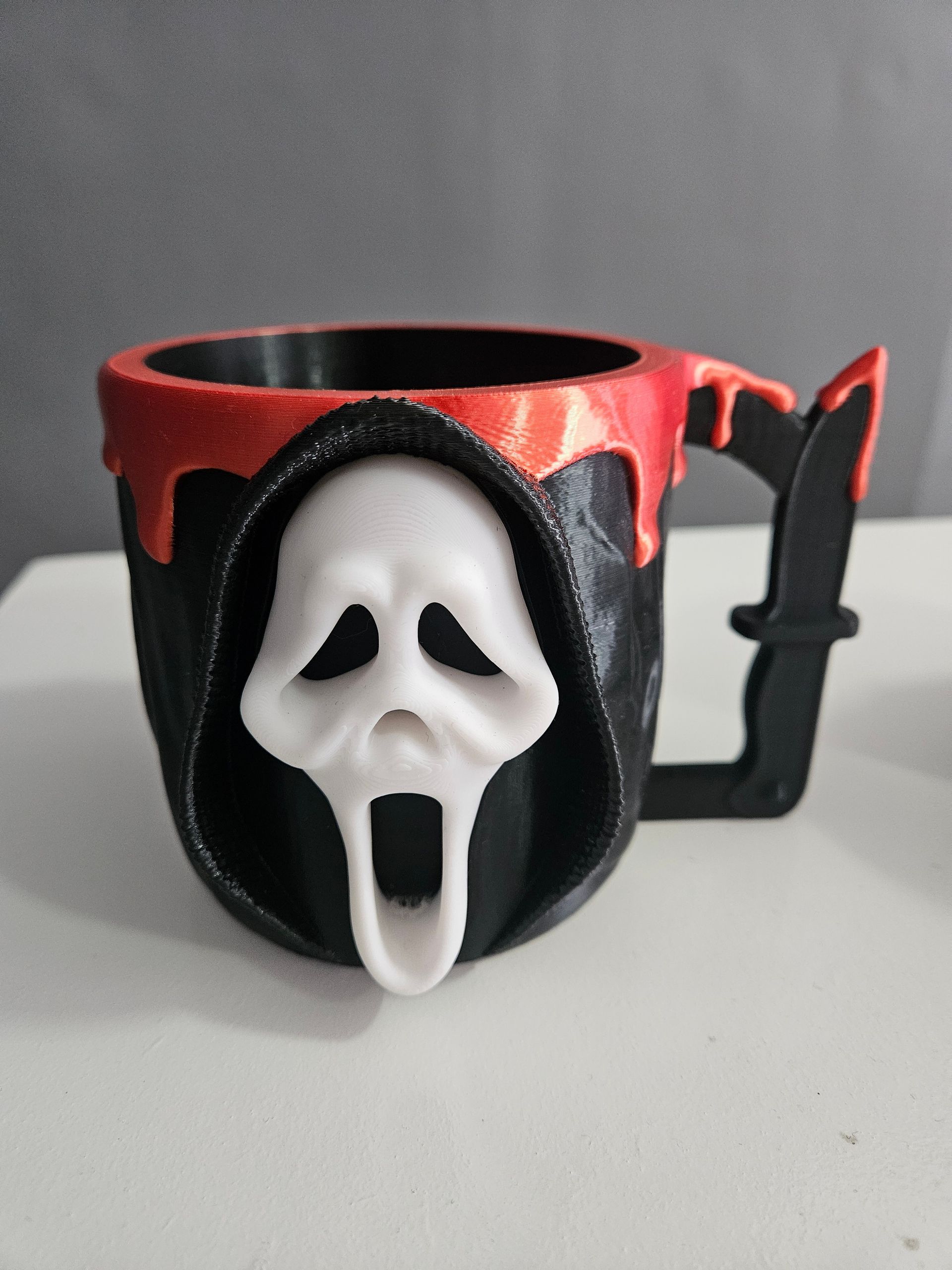 Black-and-red Ghostface mug with a handle, featuring a white screaming mask on the front