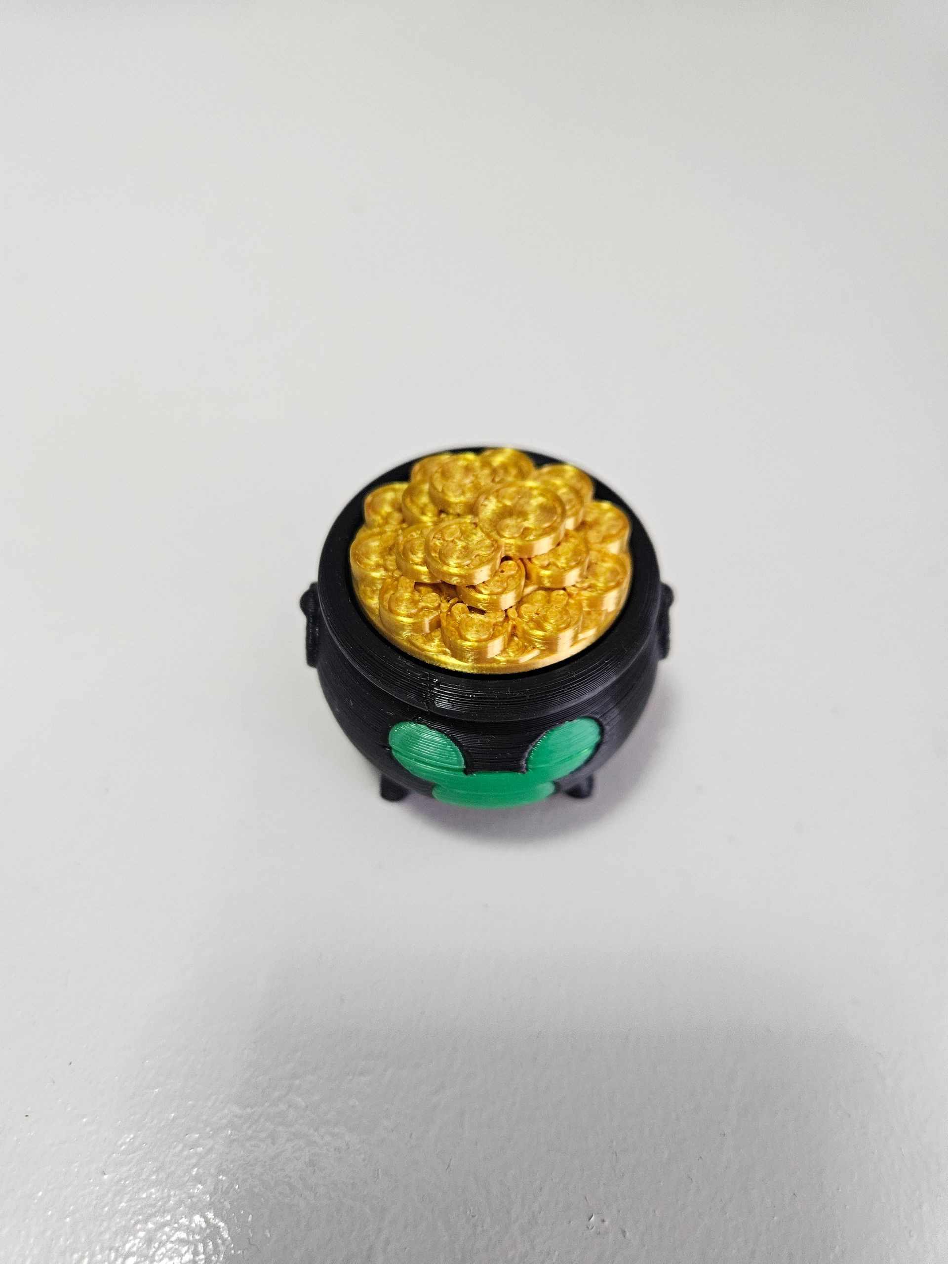 Small black cauldron filled with gold glitter, with green accents on a white background