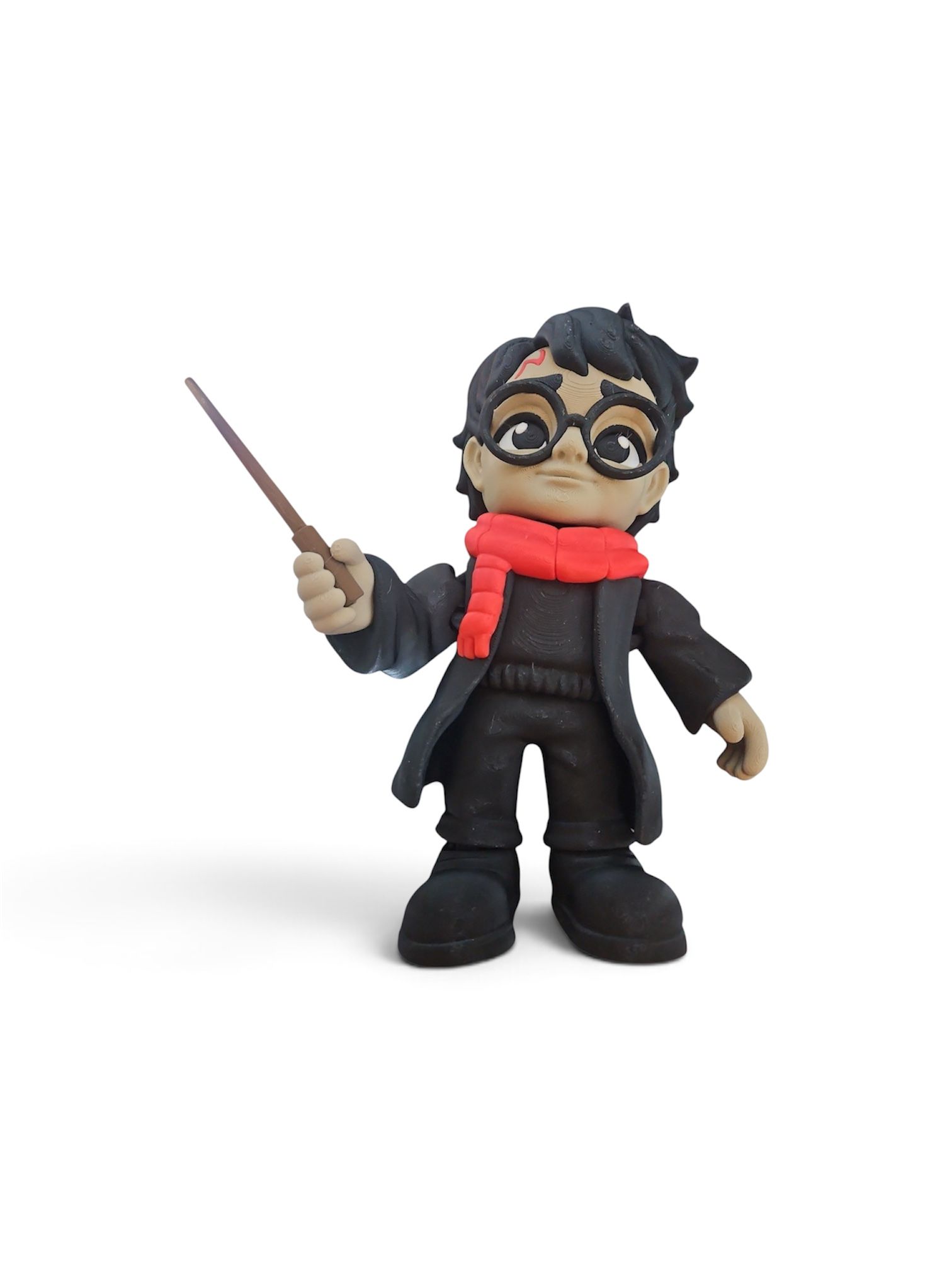 Small toy wizard with glasses, black robes, red scarf, and wand raised against a white background