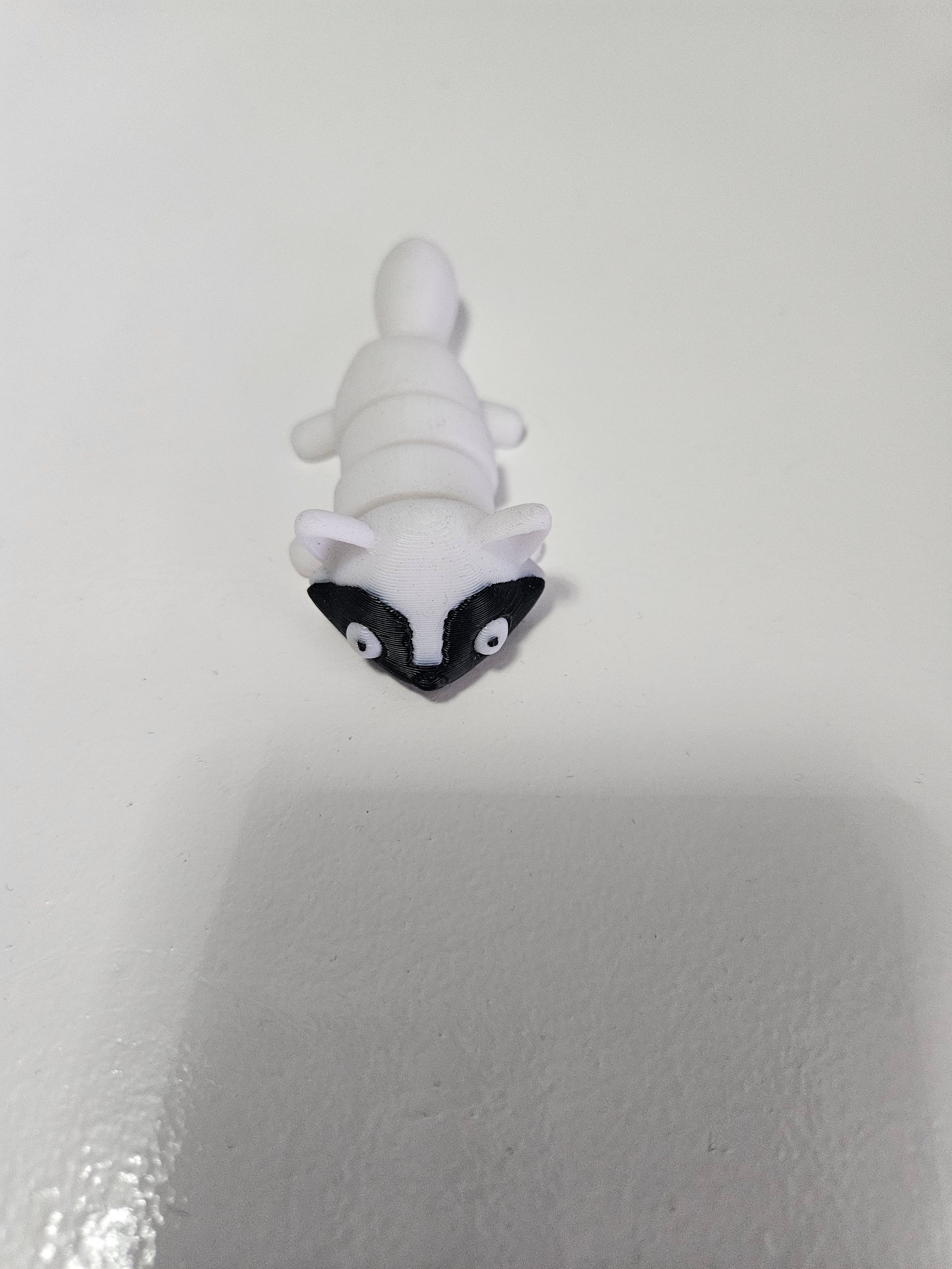 Small white raccoon figurine with black mask and eyes on a white surface.