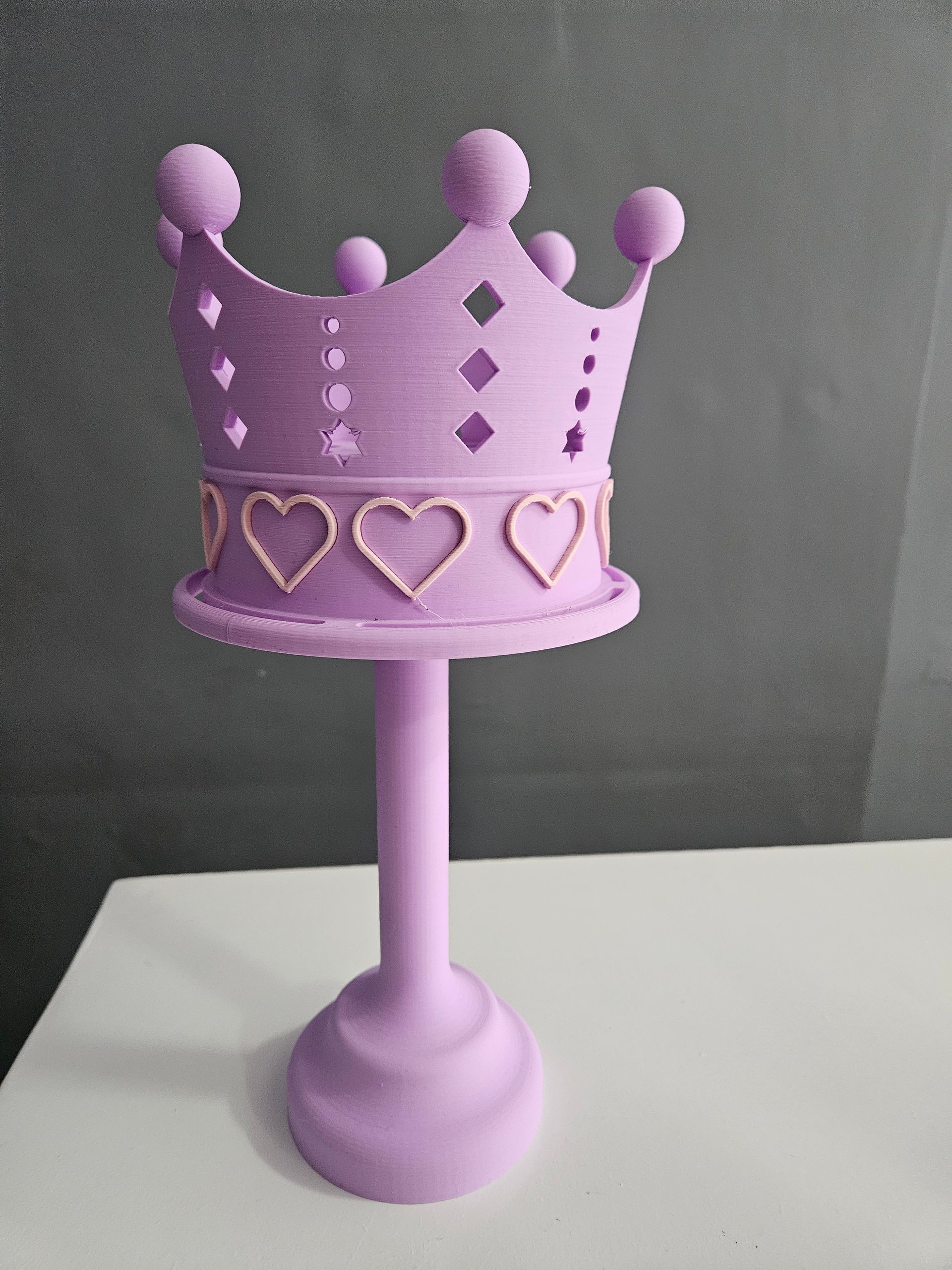 Purple crown-shaped cake stand with heart and diamond cutouts, sitting on a white surface.