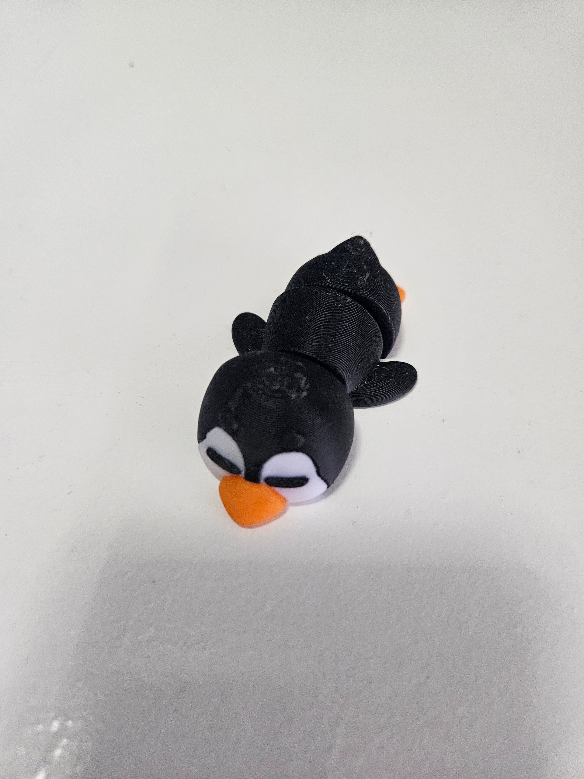 Black and white penguin toy with orange beak, lying on its side.
