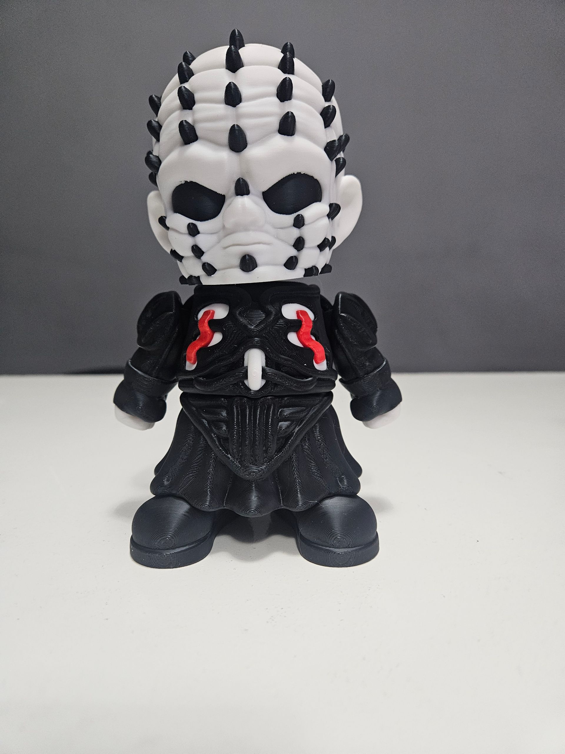 Pinhead figurine from Hellraiser, black outfit, white head with black pins, standing.