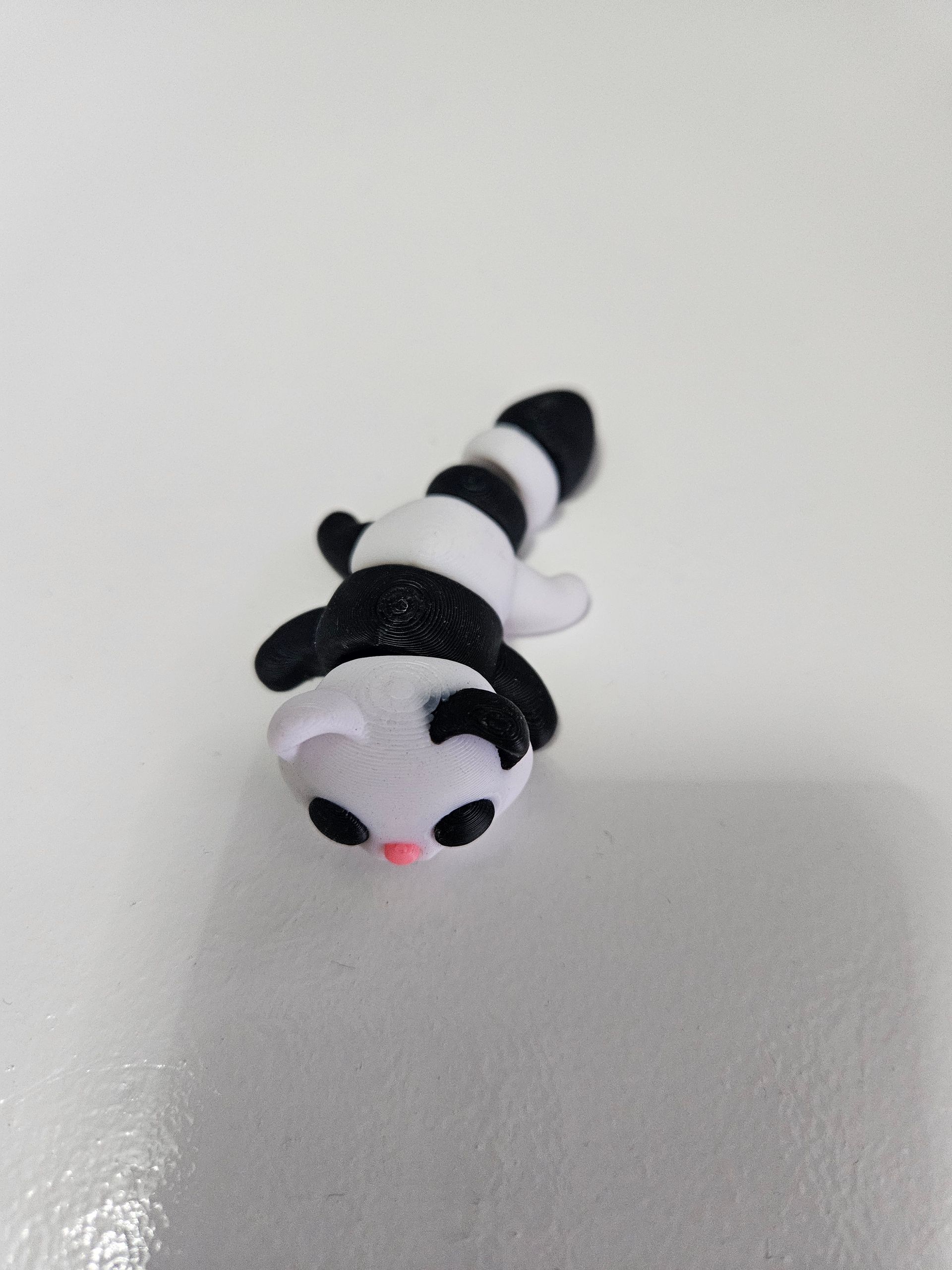 Small, black and white panda figurine with pink nose and small paws, lying down on white surface.