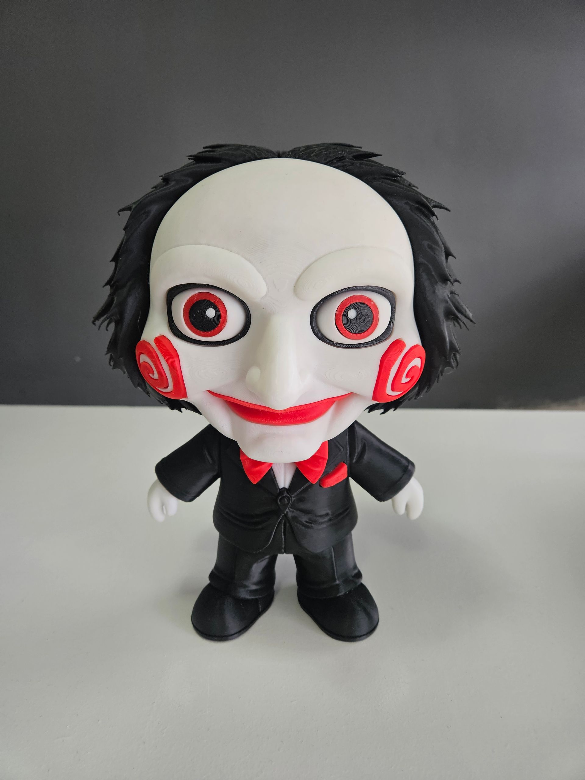 Small plush doll with white face, black hair, red markings, and black outfit standing on a plain surface