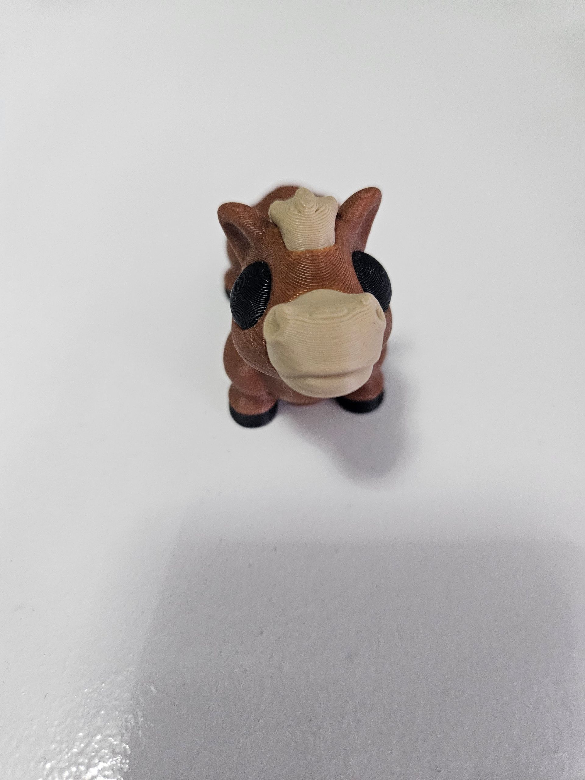 Brown and white toy horse with black eyes and hooves on a white surface.