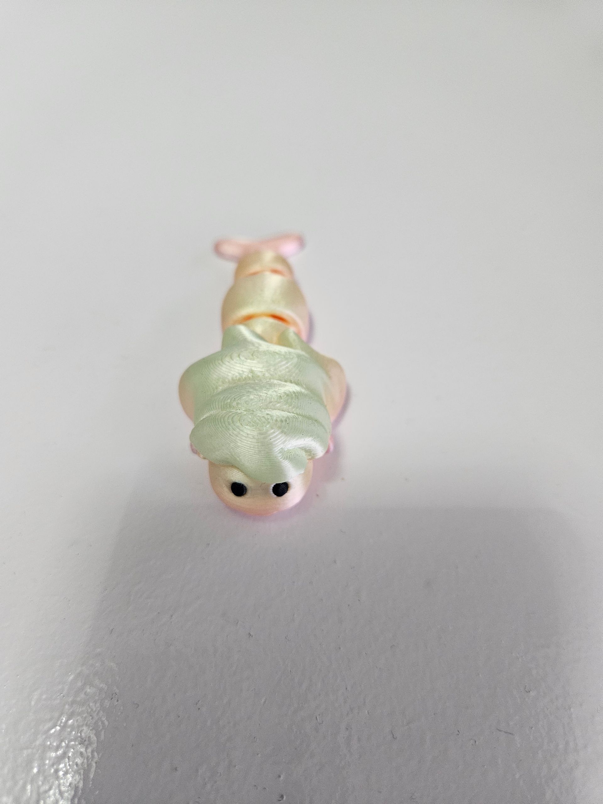 A small, pastel-colored snail figurine on a white surface with green