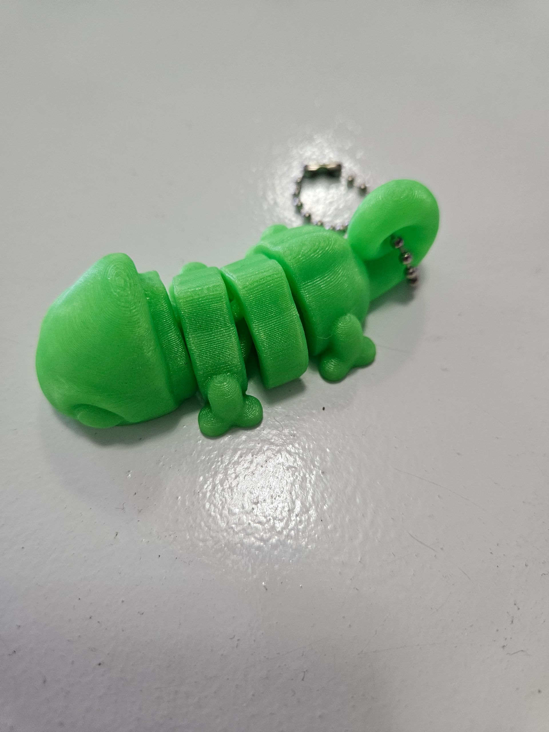 Green, articulated, 3D-printed lizard keychain on a gray surface.