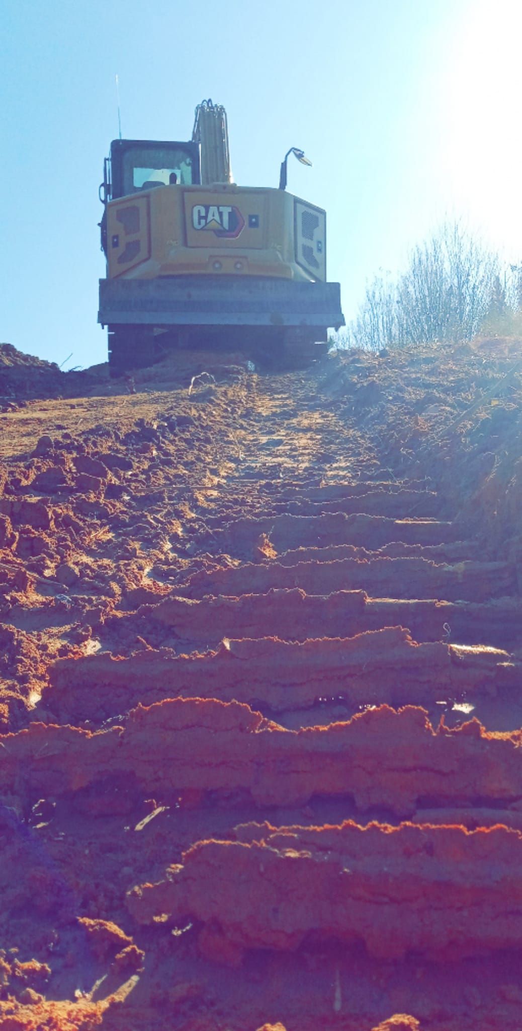 A Caterpillar bulldozer on a reddish-brown dirt slope against a bright blue sky.