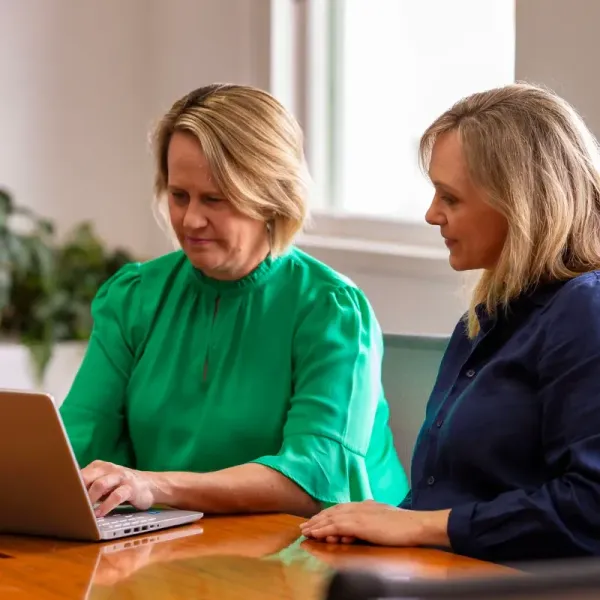 Two women are sitting at a table looking at a laptop computer.