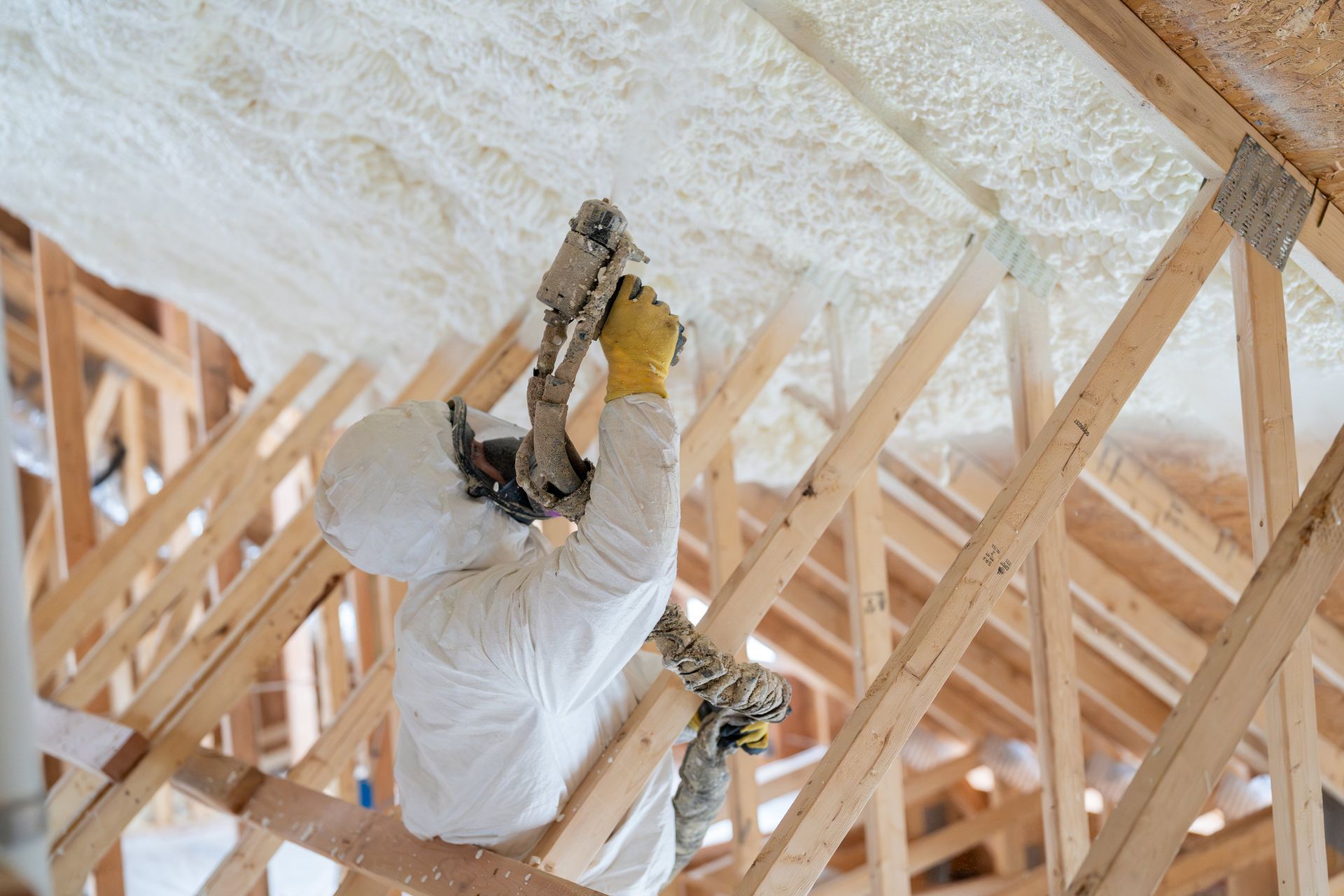 A worker wearing a mask and protective suit is spraying a house with foam insulation. A worker wearing a mask and protective suit is spraying a house with foam insulation.