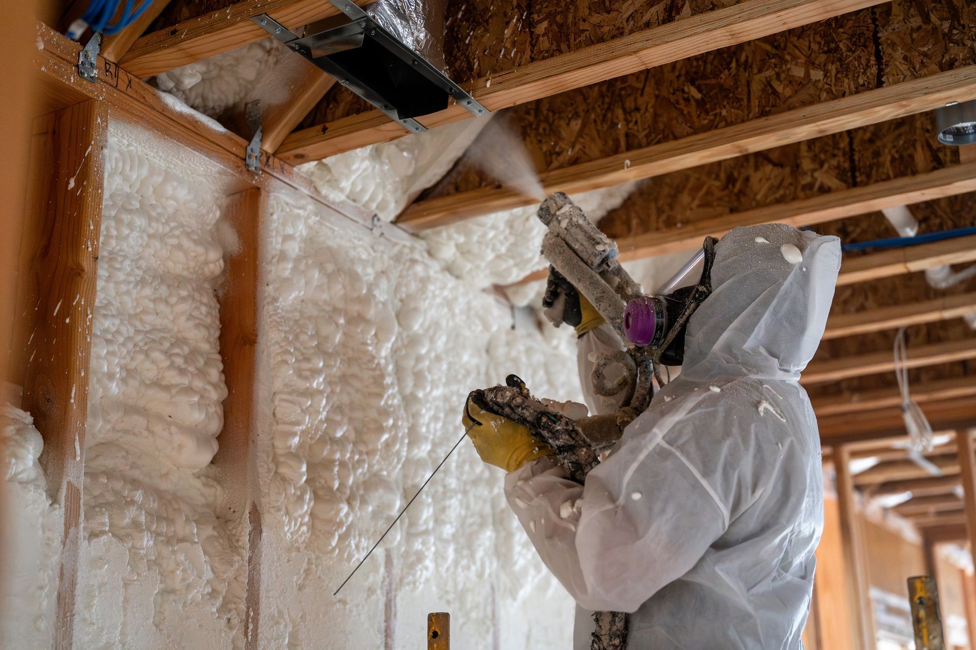 Worker in full gear spraying foam insulation in building under construction.