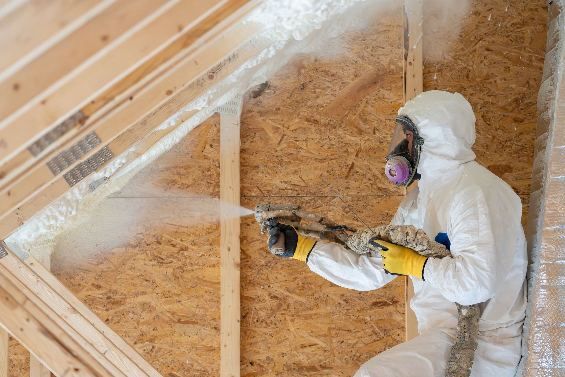 A worker spraying foam insulation on an attic ceiling.