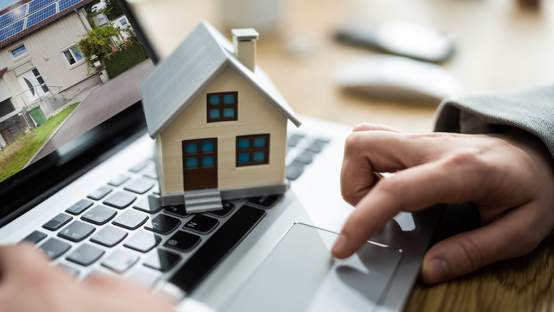 Person using laptop with a model house sitting on the keyboard, real estate website displayed.