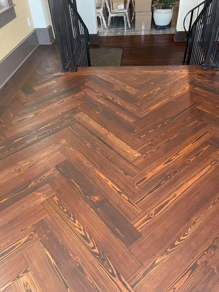 Herringbone wood floor with a dark border leading to a doorway and stair landing