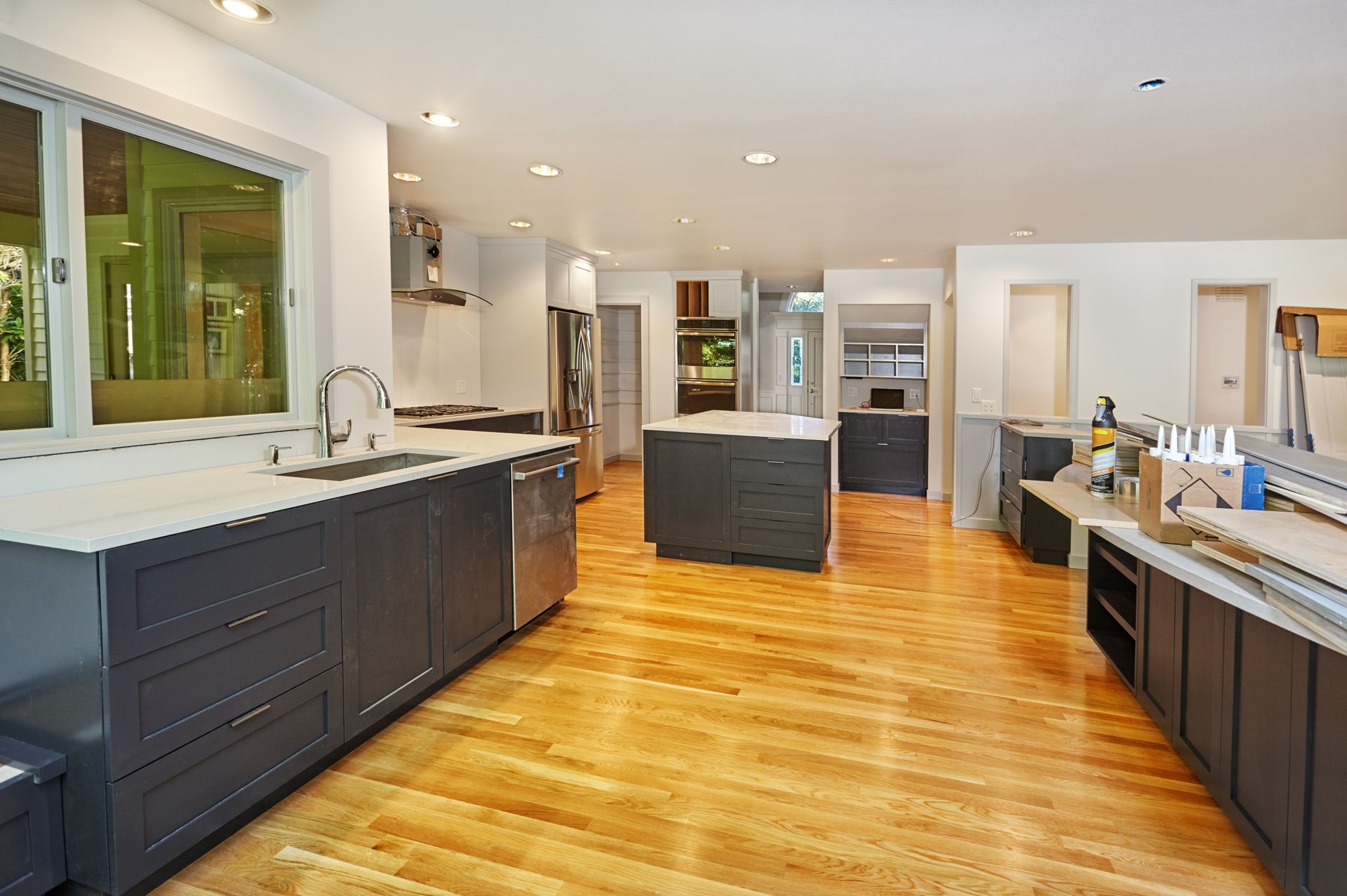 Modern kitchen with dark cabinets, wood floors, white countertops, and stainless steel appliances