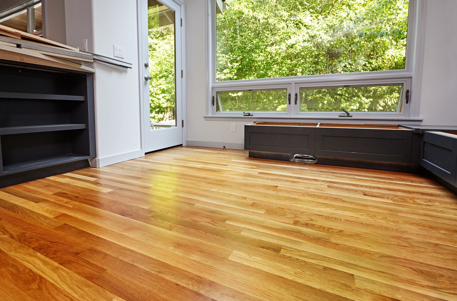 Empty room with hardwood floor, black shelving, and large windows overlooking greenery
