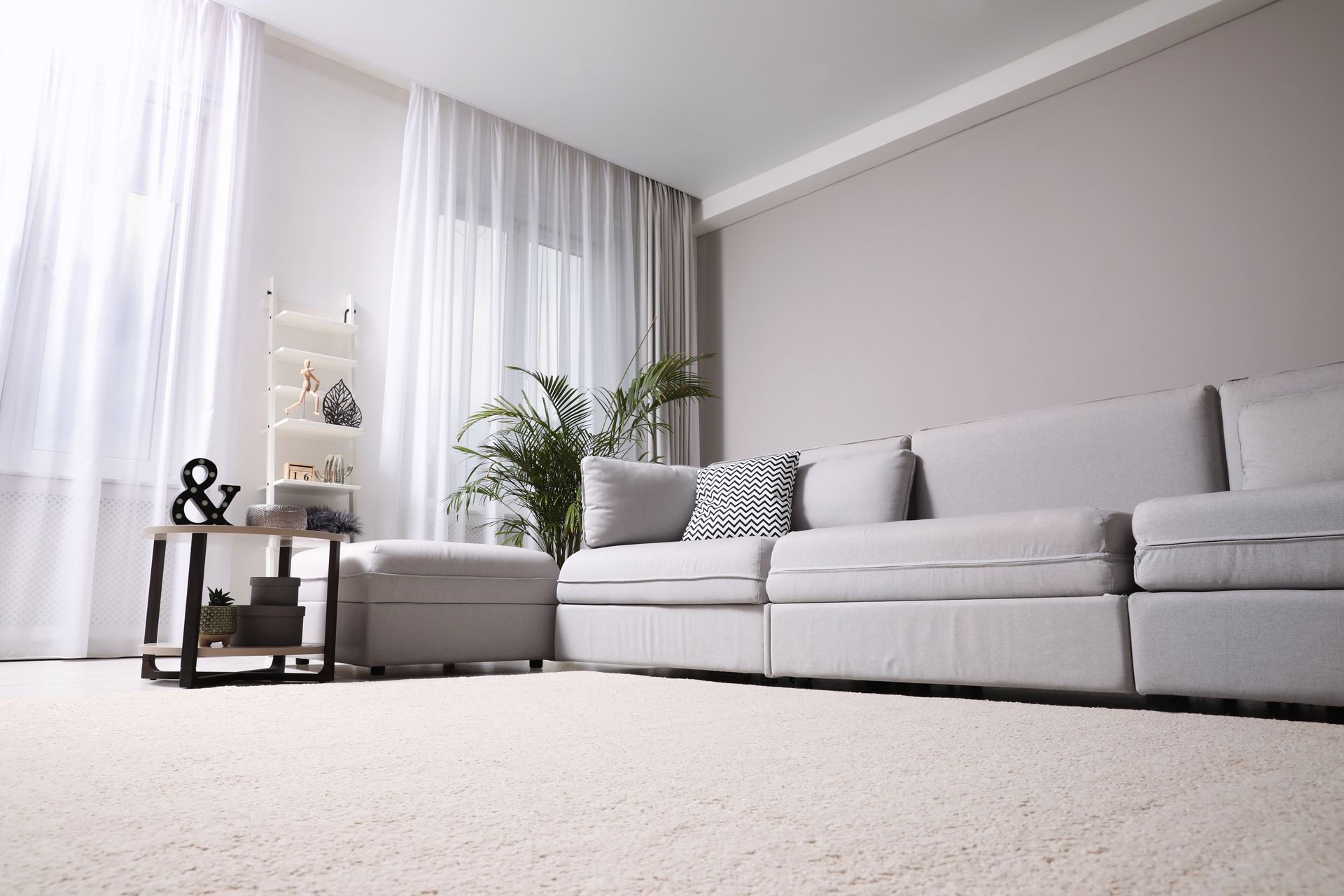 Bright living room with a gray sofa, white curtains, and a light rug