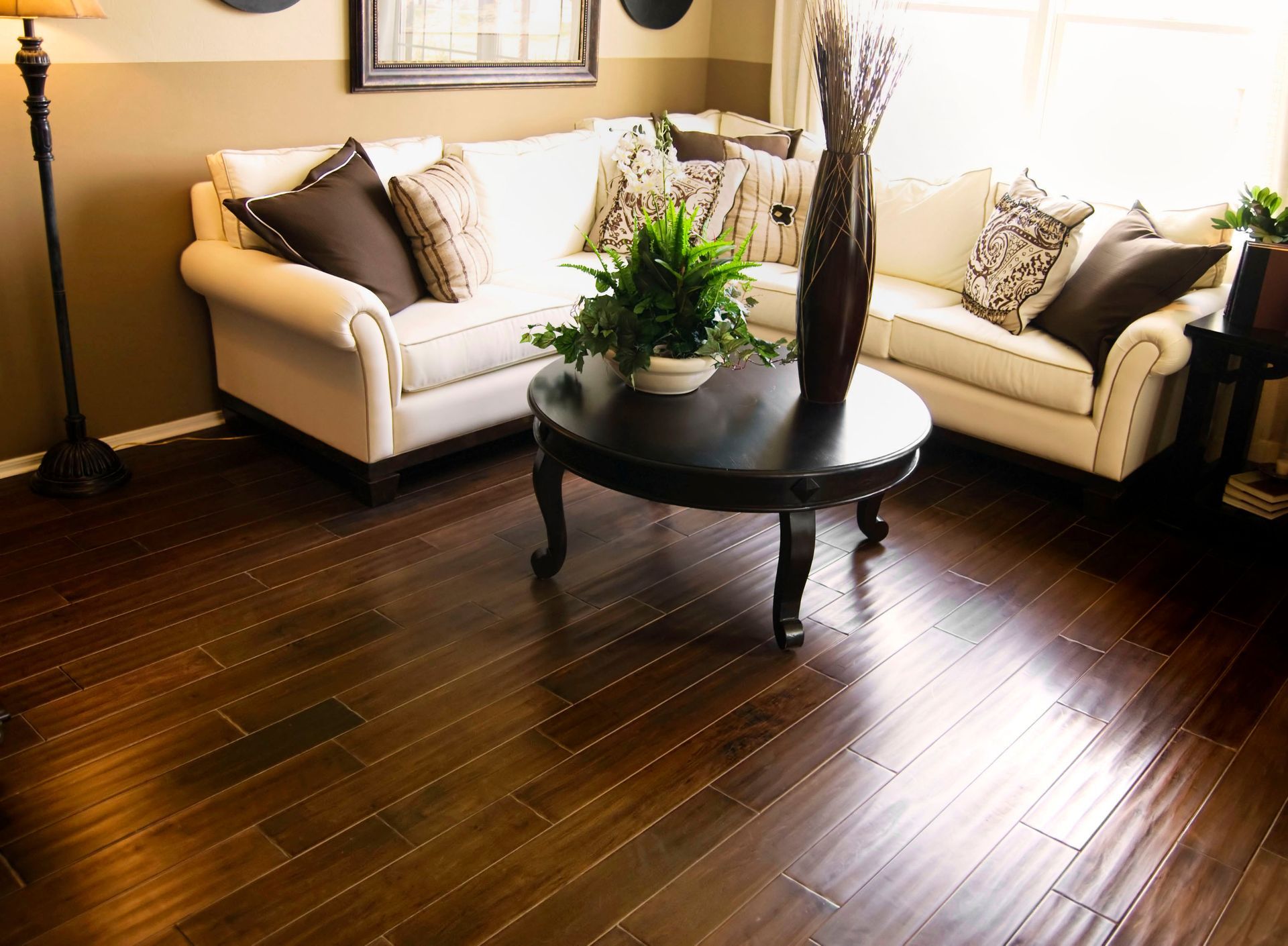 Bright living room with white sofas, dark wood floors, and a round coffee table with a plant.