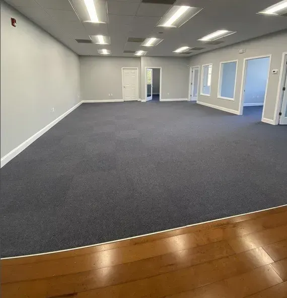 Empty office space with gray carpet, white walls, and wood flooring in front