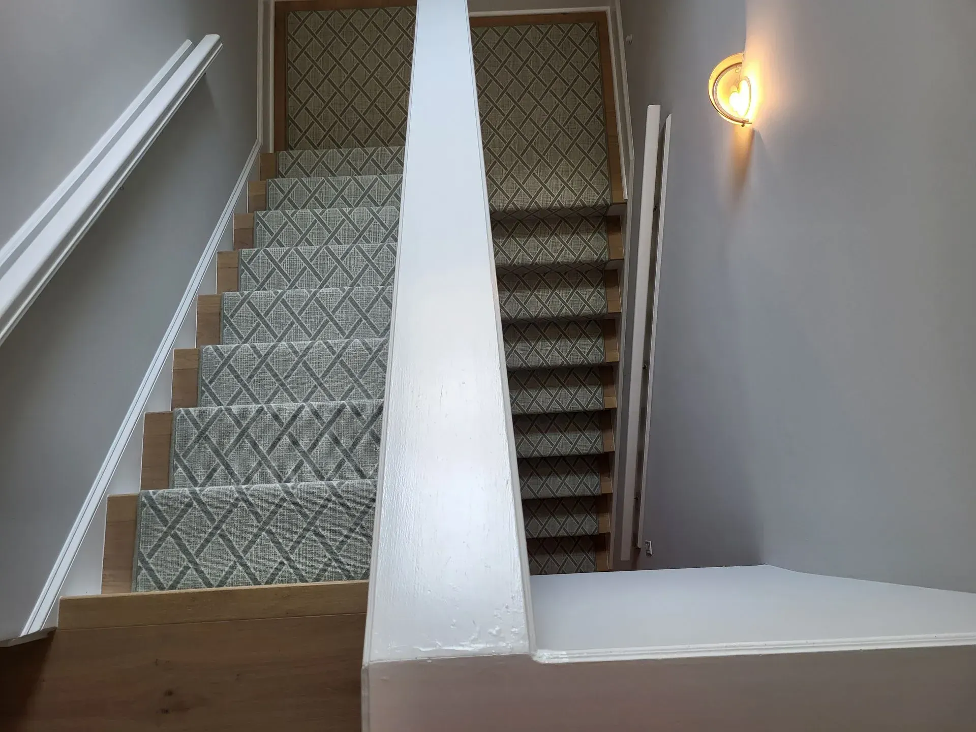 Stairwell with patterned carpeted stairs, white walls, and a lit wall sconce.