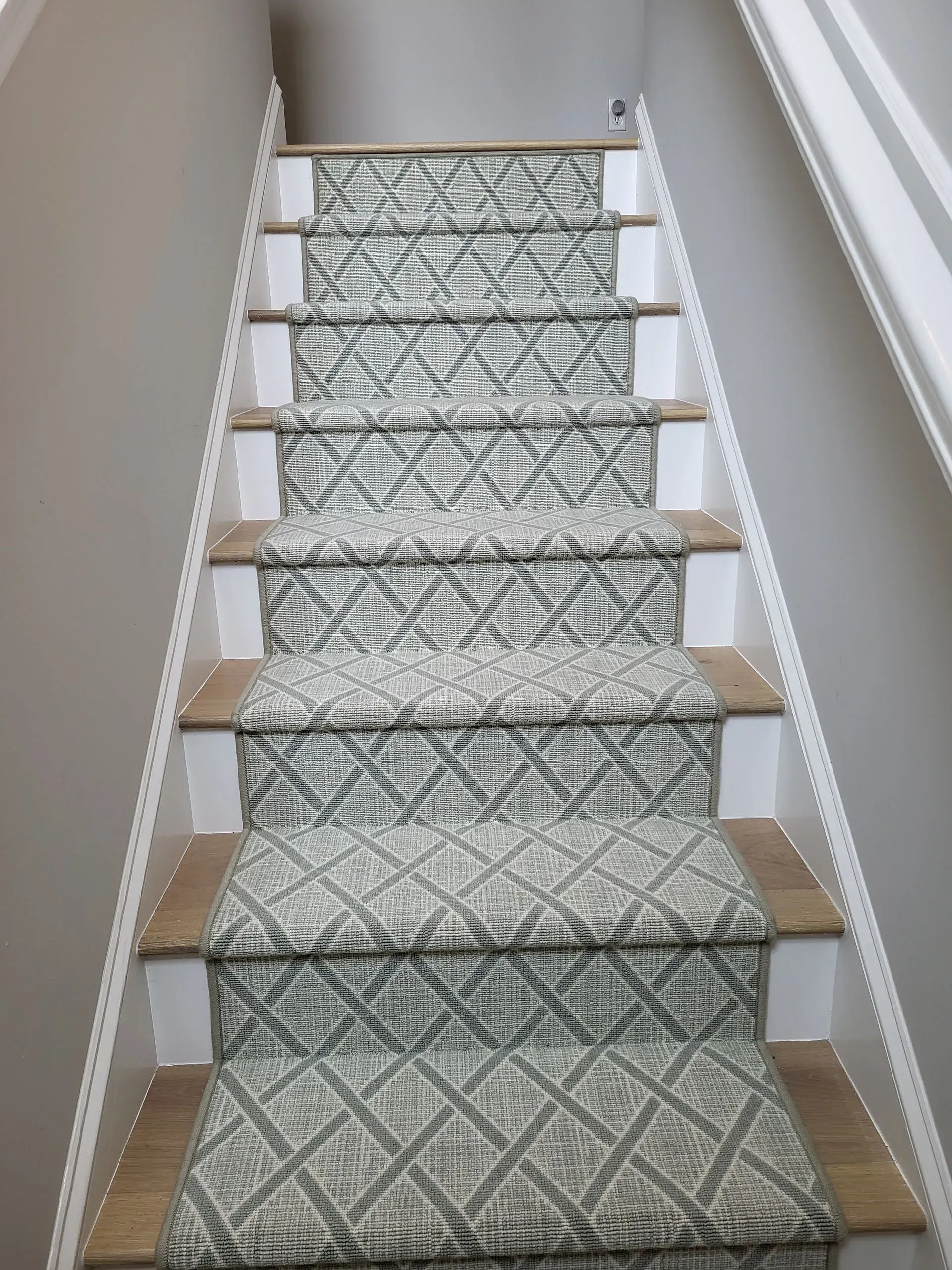 Patterned carpet runner on a narrow staircase with white walls and wooden steps