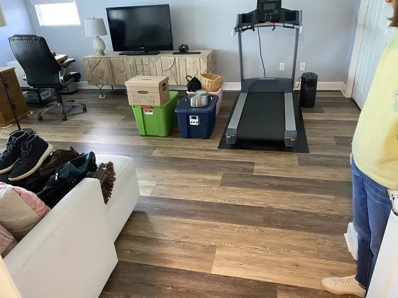 Living room with treadmill, TV, couch, and storage bins on a wood floor