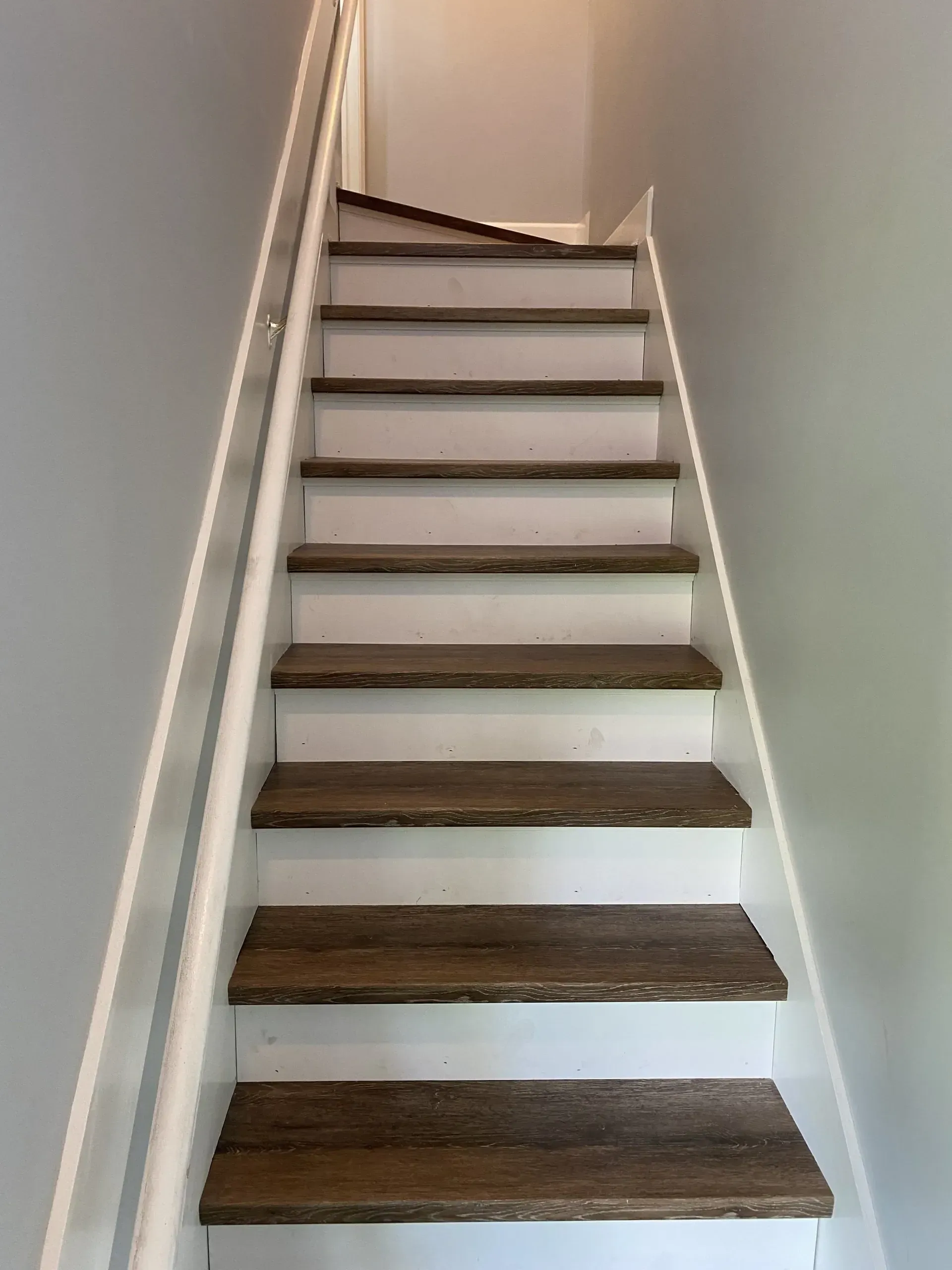 Narrow indoor staircase with white railings and dark wooden steps viewed from below