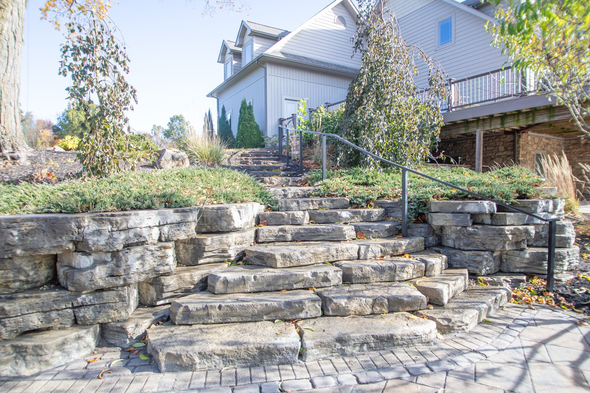 Stone steps leading up to a two-story building with a wooden deck; shrubs and a metal handrail are also visible.