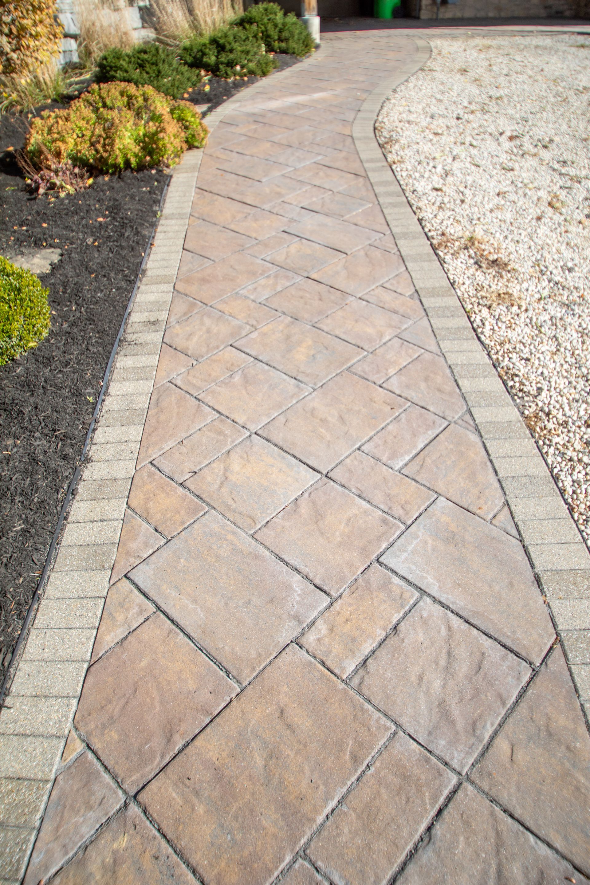 Stone pathway with patterned pavers and border, leading towards a driveway.