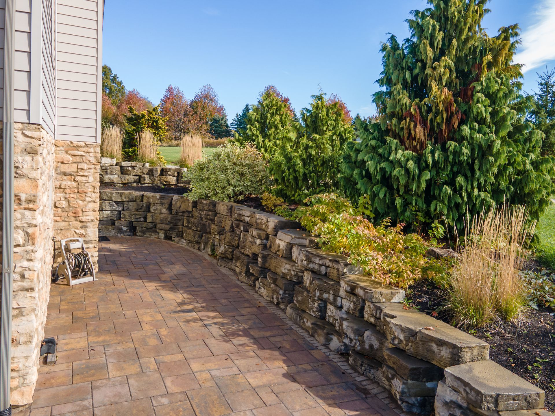Stone patio and retaining wall with colorful plants and green shrubbery.