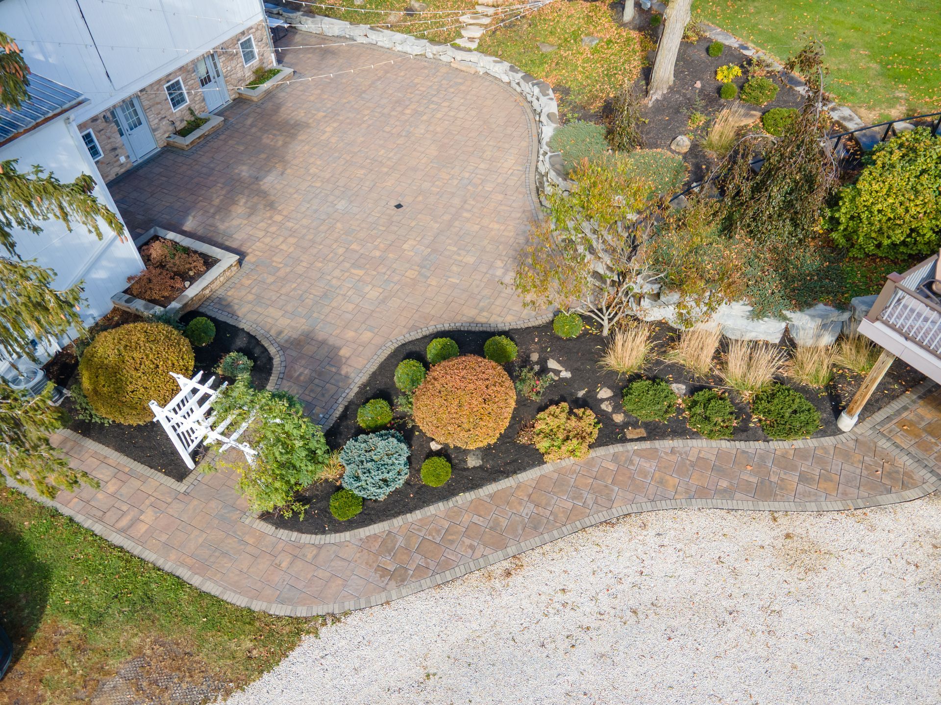 Overhead view of a brick driveway and landscaped garden with various plants and a gravel path.
