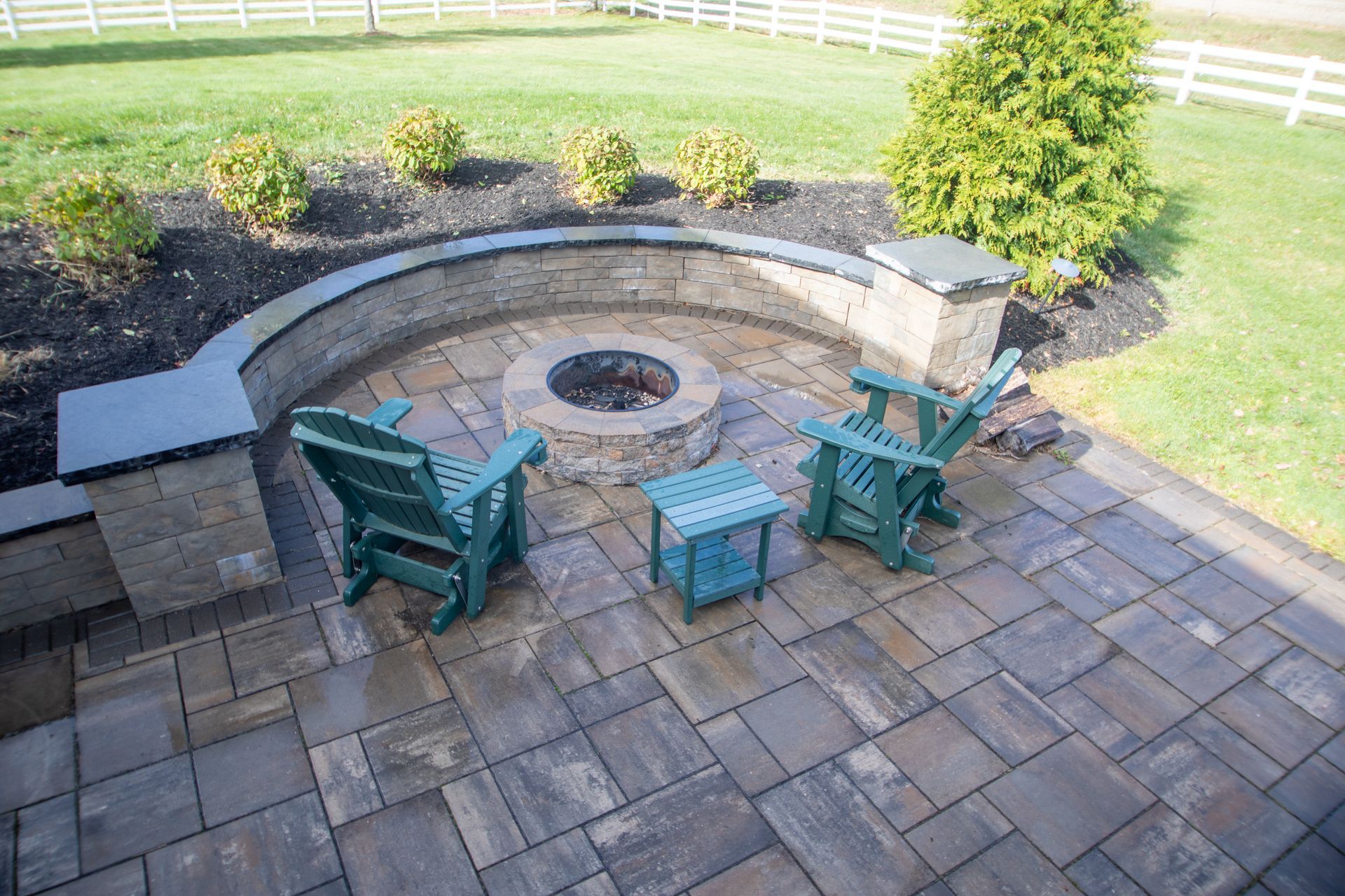 Stone patio with a fire pit, two green chairs, and a small table.