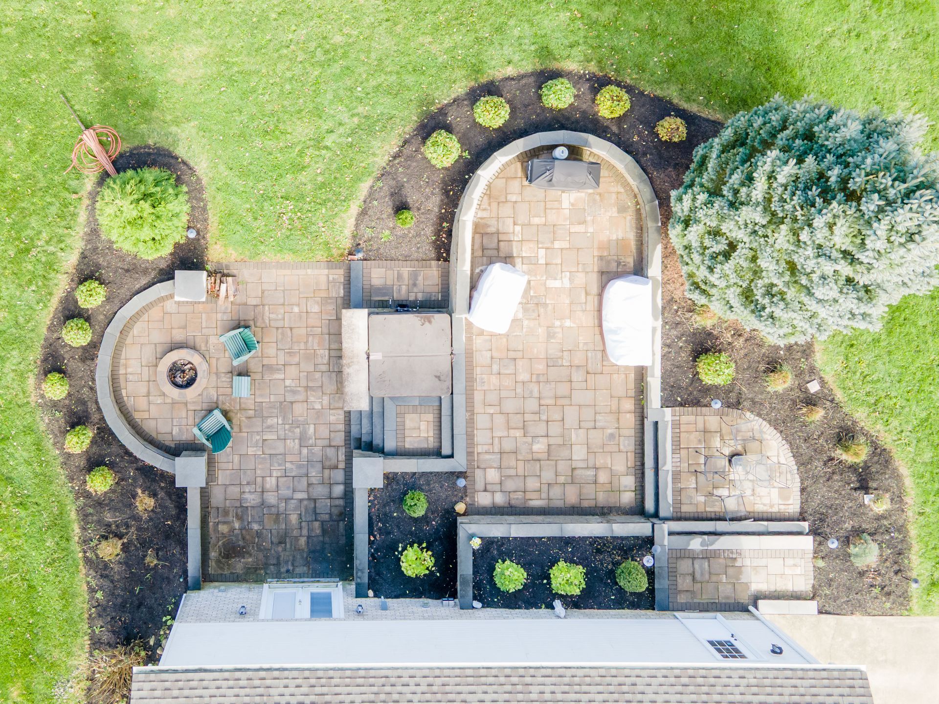 Overhead view of a backyard patio with a fire pit, seating, and landscaping with green grass.