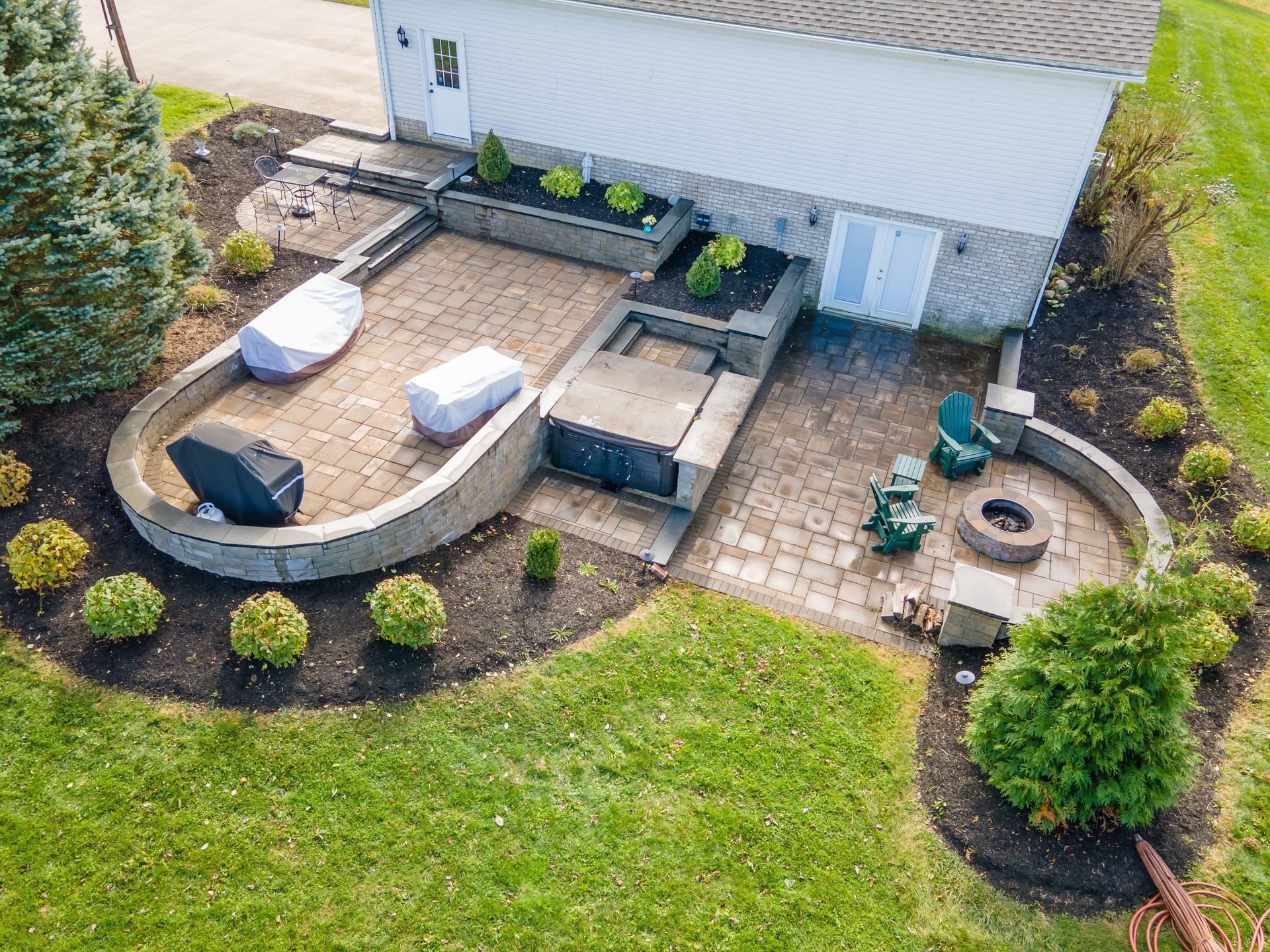 Multi-tiered paver patio with seat wall, fire pit, hot tub and grill. Backyard with landscaping.