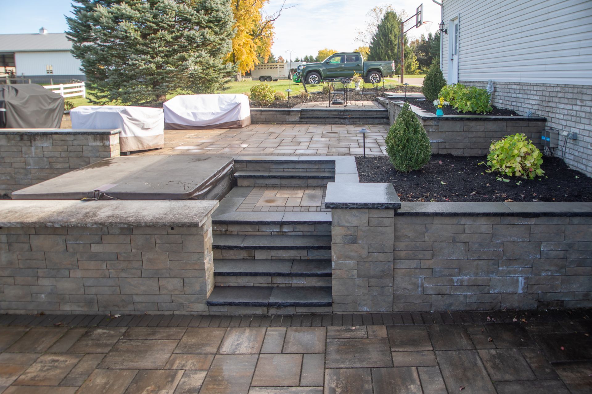 Stone patio with retaining walls, steps, and shrubs. A truck is parked in the background.