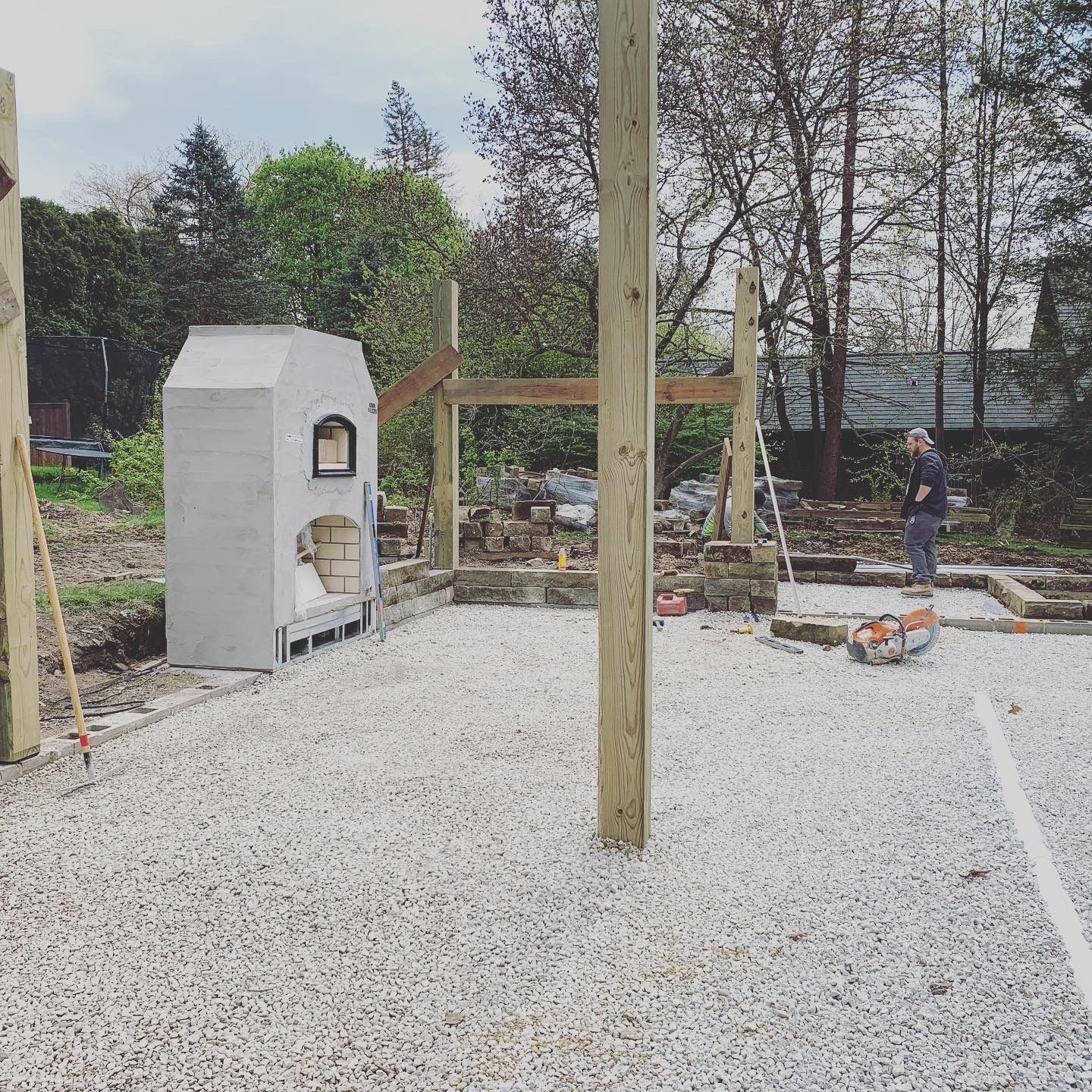 Construction site with a stone oven, wooden beams, gravel, and a person working outdoors.