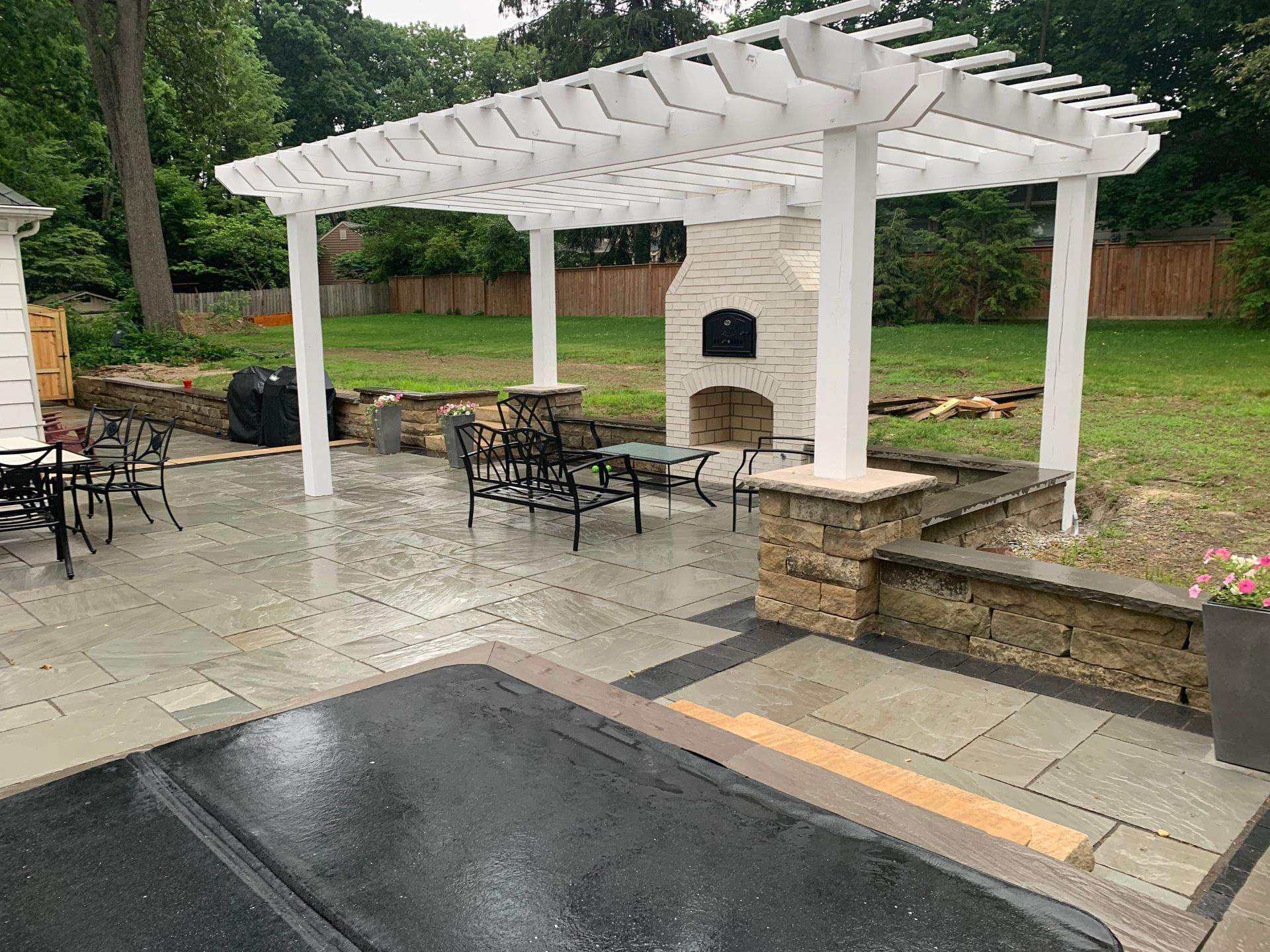 Patio with white pergola, outdoor fireplace, stone walls, seating, and hot tub cover.