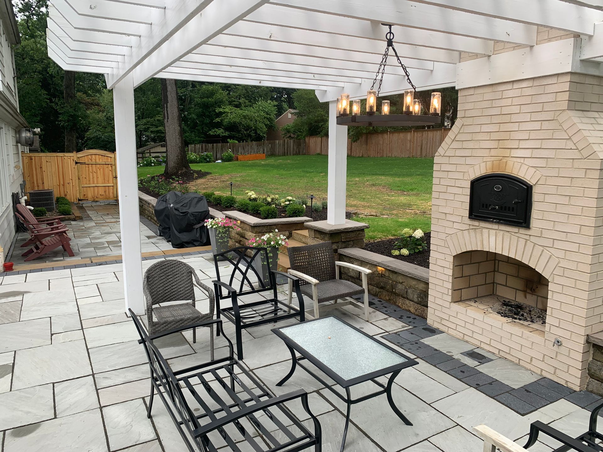 Patio with pergola, fireplace, and seating area. Overlooks a backyard with a wooden fence.