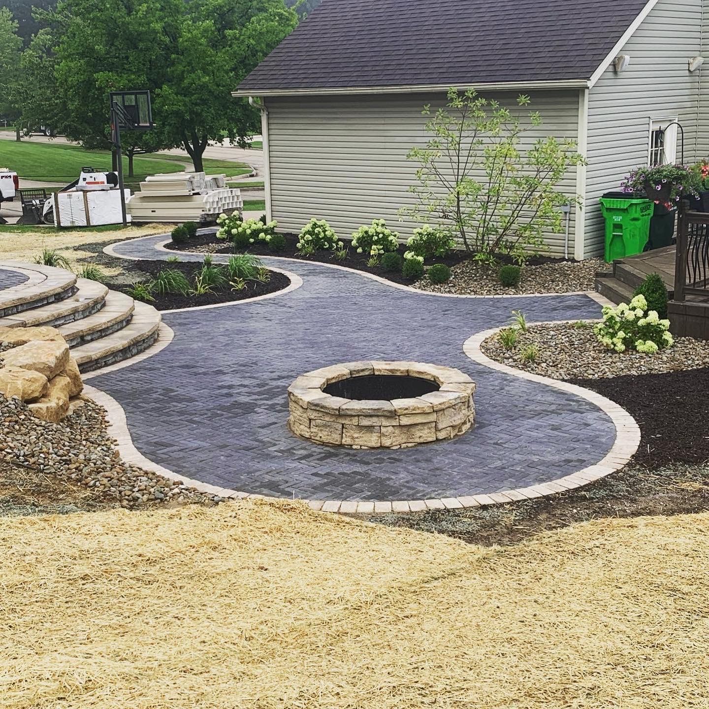 Backyard patio with fire pit, stone steps, and landscaping featuring a gray gravel surface and beige edging.