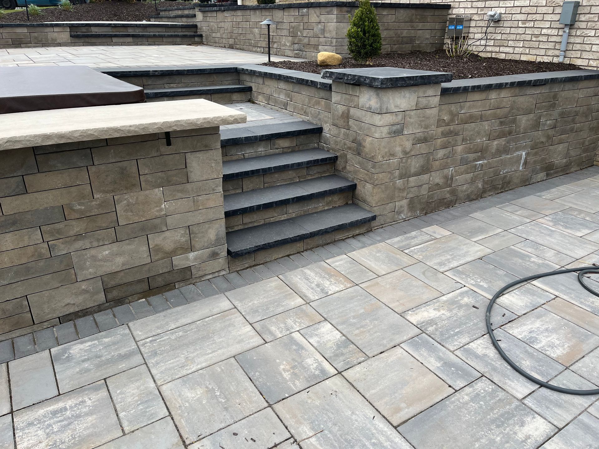 Stone patio with steps and retaining walls; gray and black blocks.