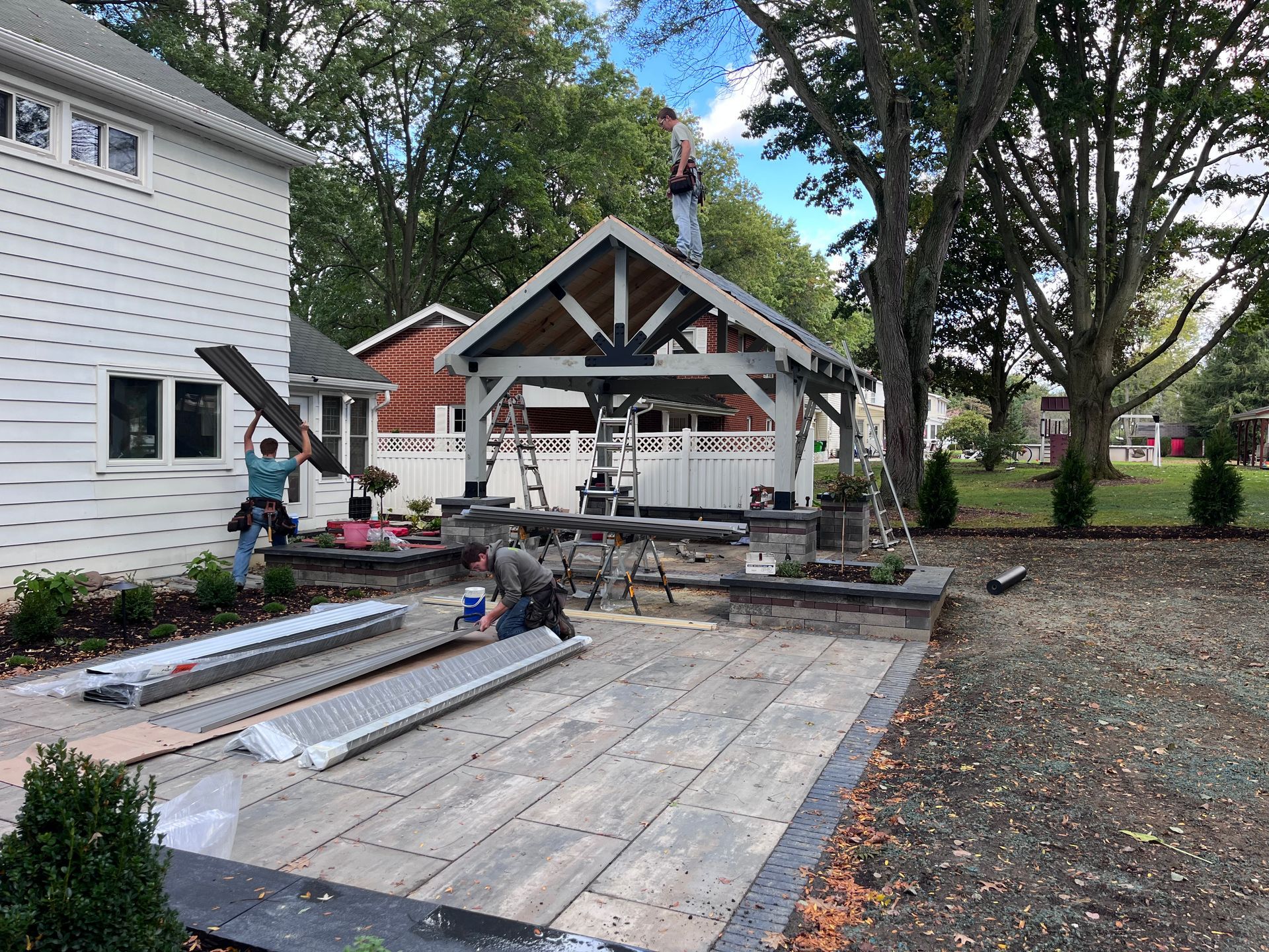 Construction workers building a wooden pavilion on a patio next to a white house.