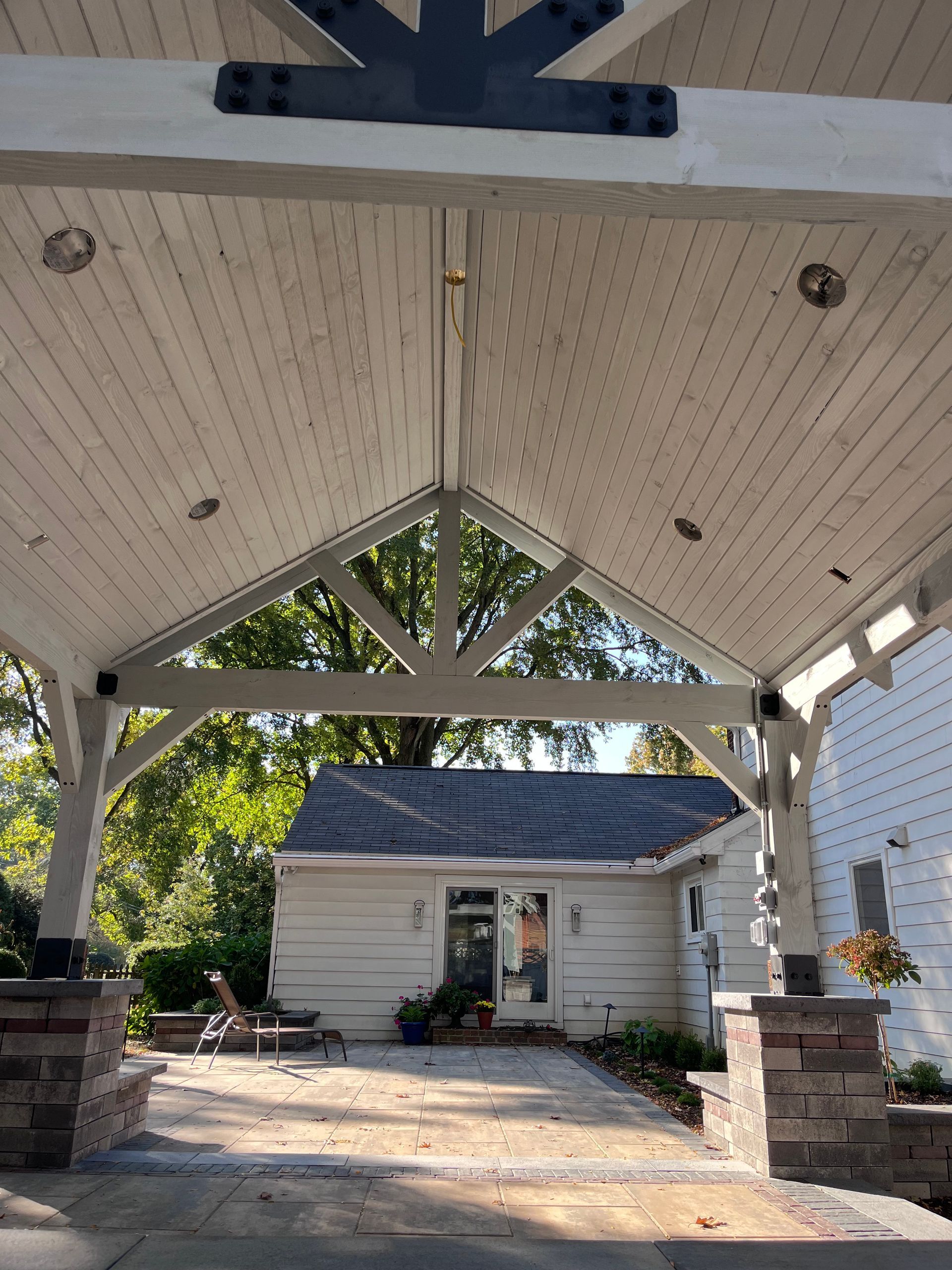 Covered entryway with white wooden beams, leading to a small building.