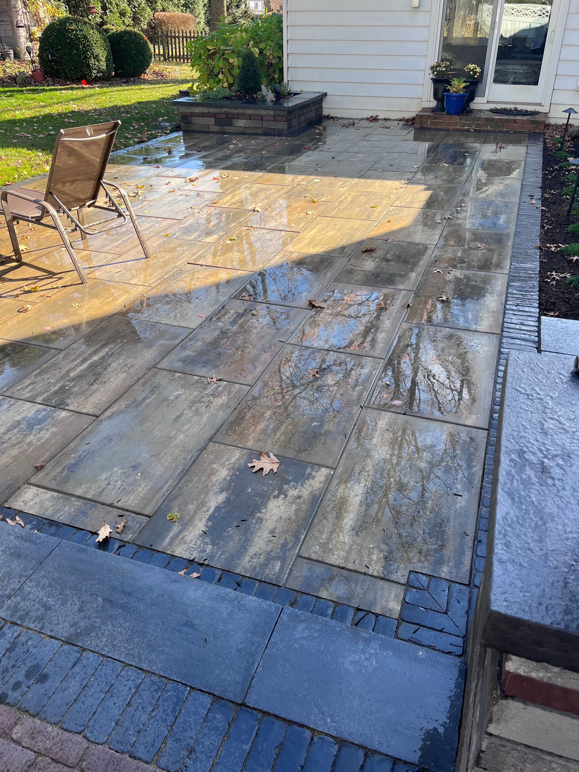 Wet stone patio with brick border and steps. Chair on the side, greenery in the background.