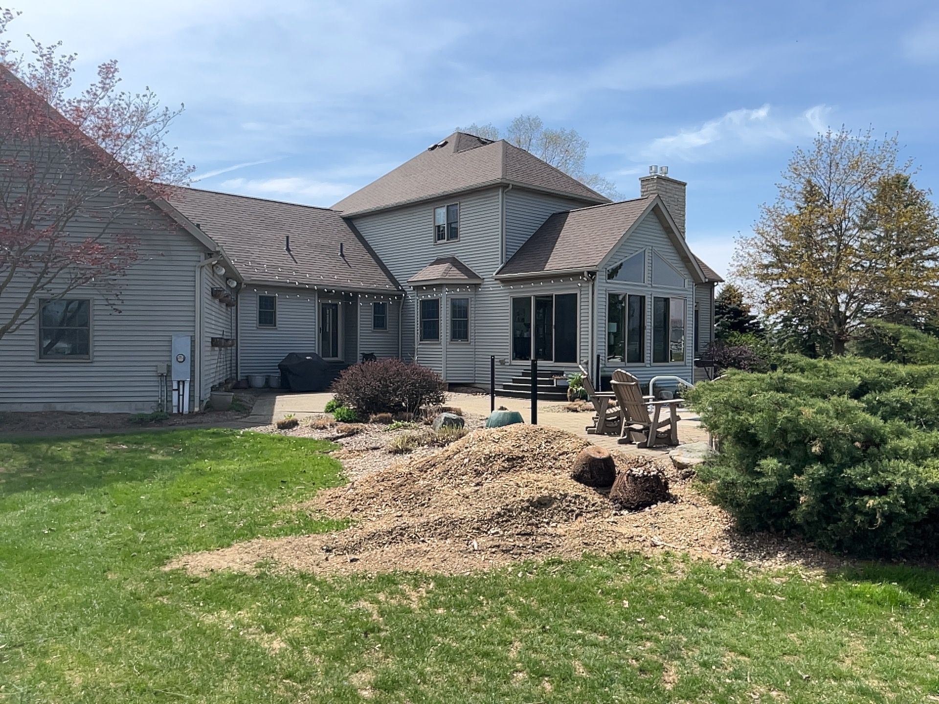 Backyard view of a two-story gray house with a patio and lawn, on a sunny day.