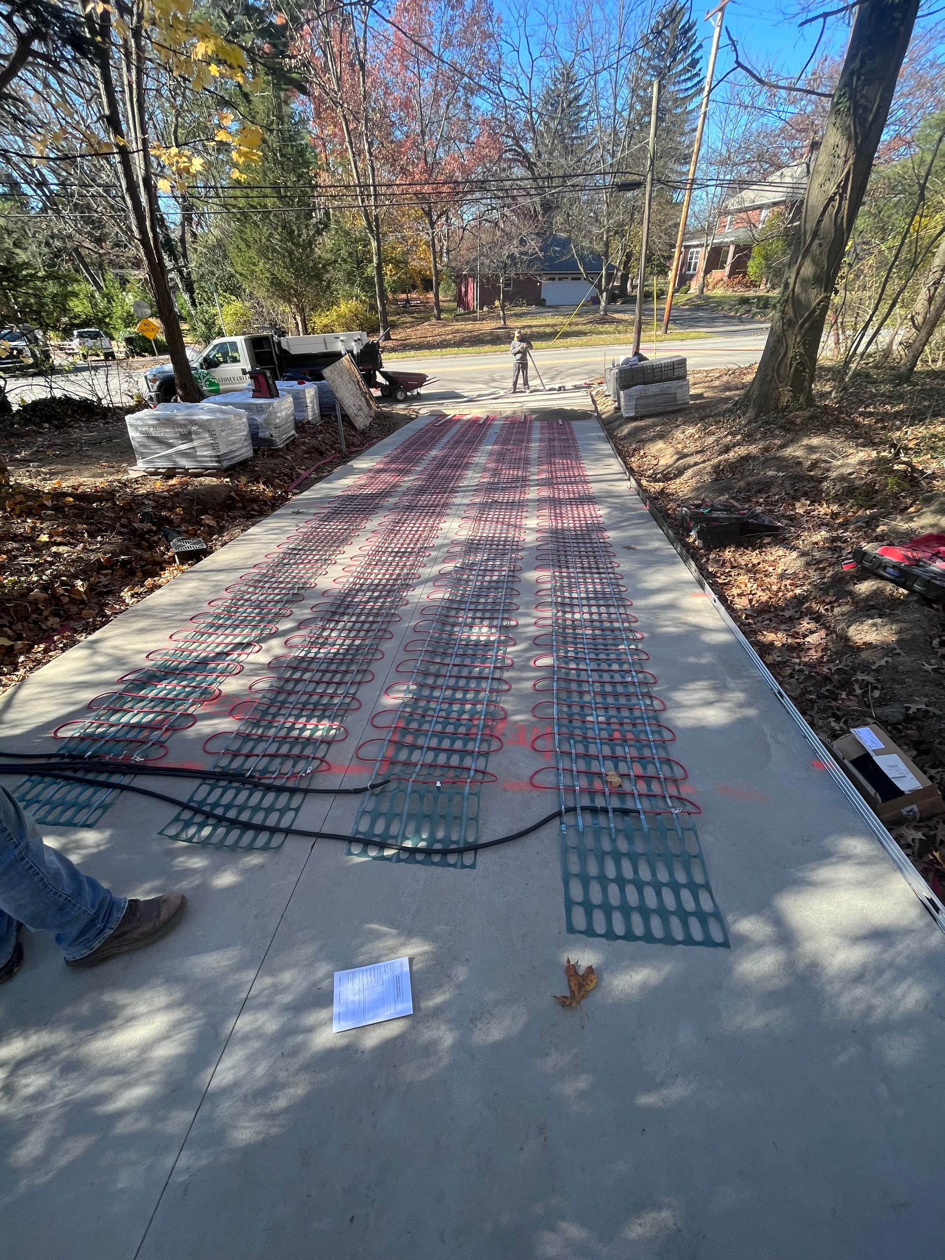 Concrete pathway with a grid of red and green components, possibly heating elements, with a person's legs visible.