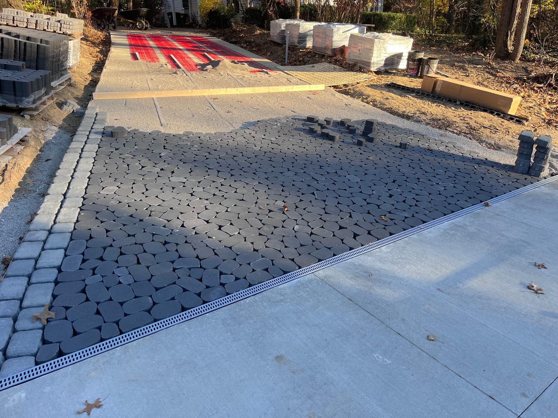 Construction site with gray pavers being installed next to concrete and other building materials.