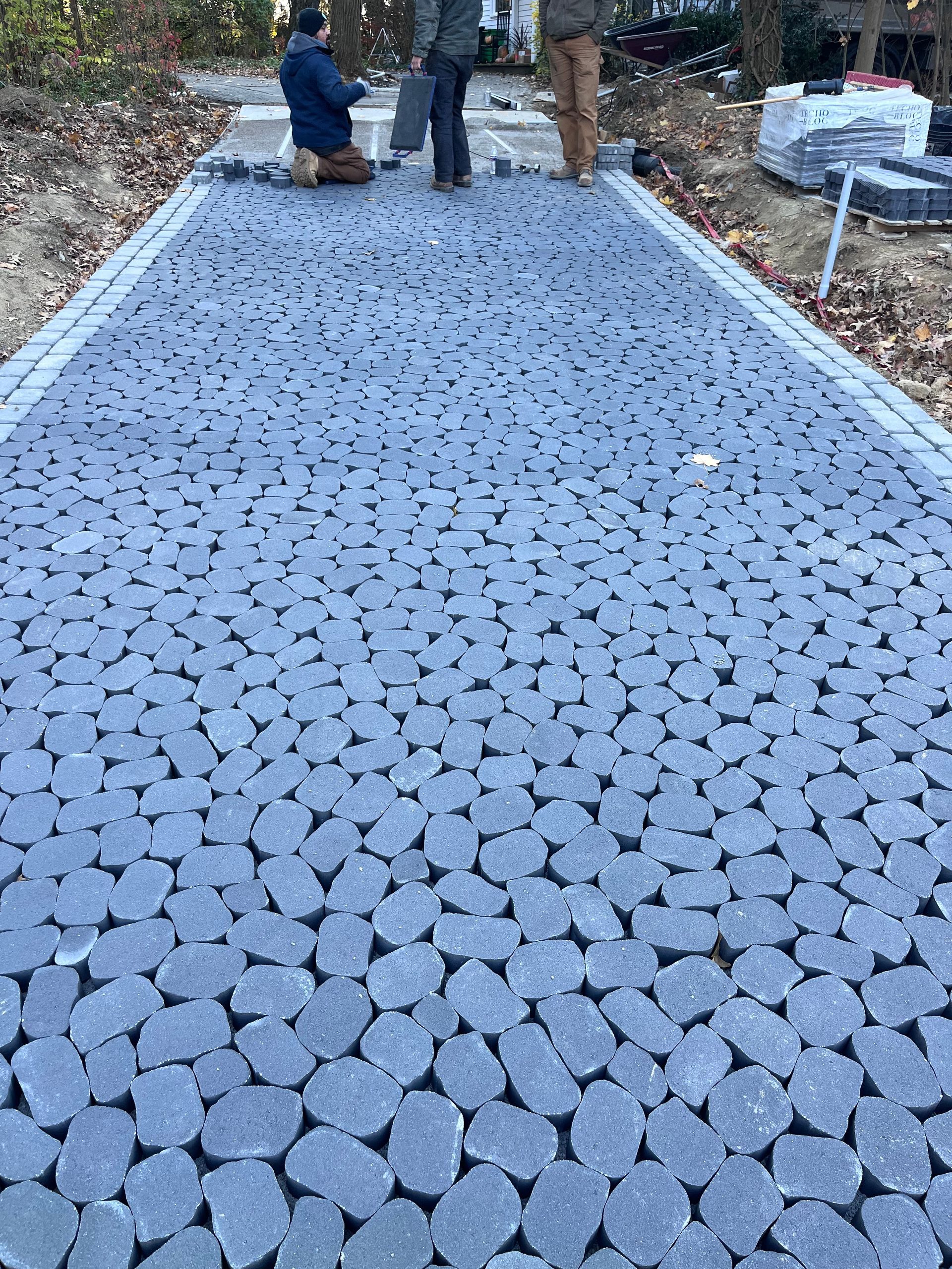 Pathway being paved with irregular gray stones, bordered by lighter paving stones. Three people are working.
